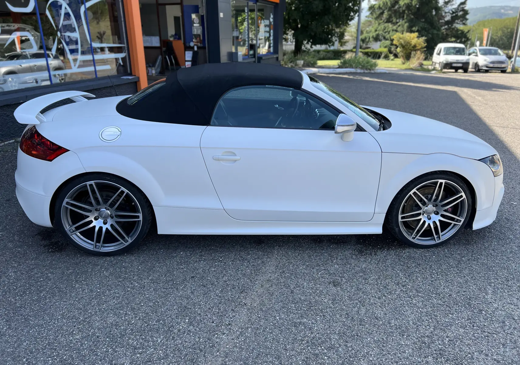 Audi TT RS Roadster blanc vue de profil côté gauche avec capote noire et jantes sport grises.