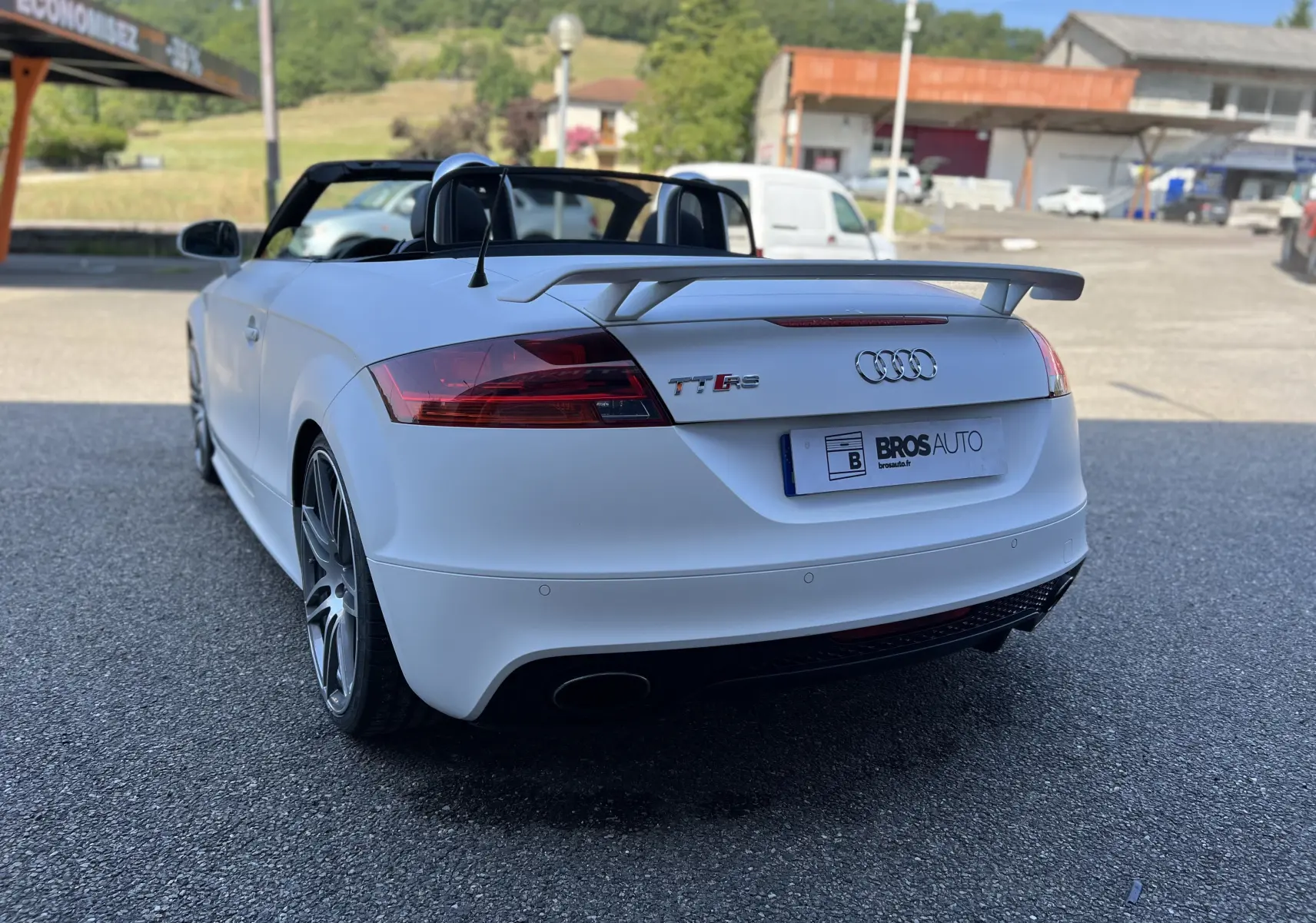 Audi TT RS Roadster blanc vu de l'arrière droit, capote ouverte et aileron arrière distinctif visible.