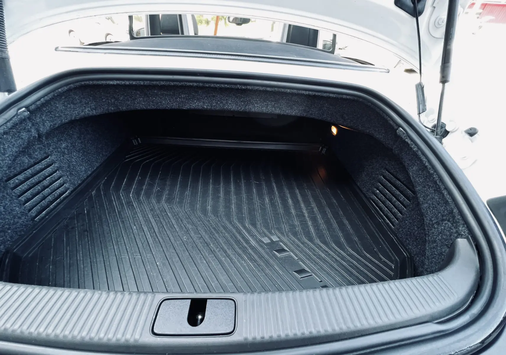 Coffre ouvert en gros plan de l'Audi TT RS Roadster blanc, montrant le tapis de protection noir et l'éclairage intérieur.