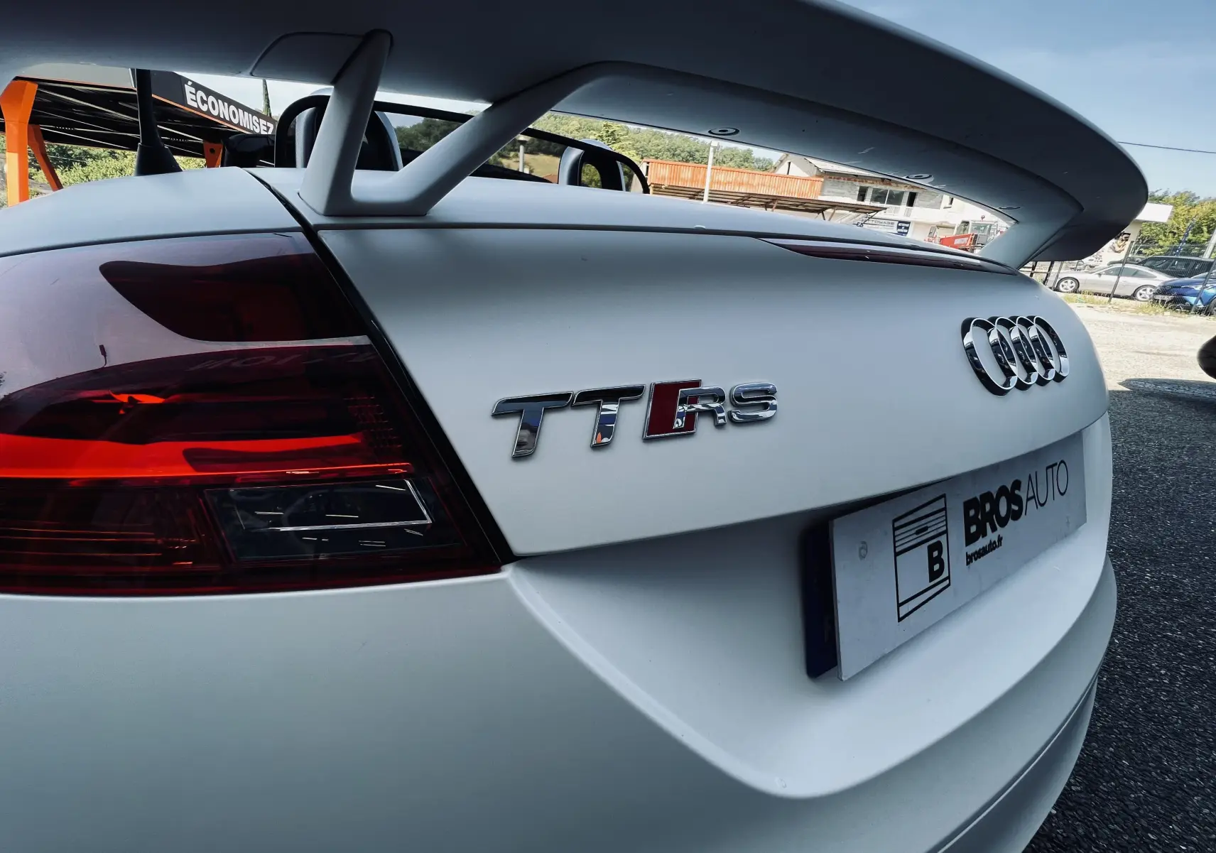 Vue arrière droite d'un Audi TT RS Roadster blanc avec son aileron et les logos distinctifs TT RS et Audi.