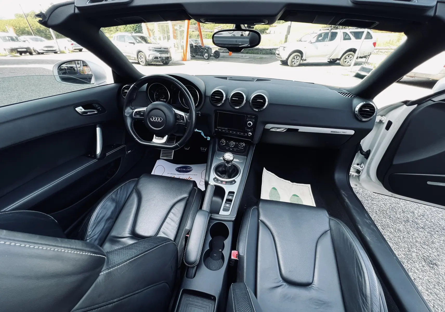 Vue intérieure frontale de l'Audi TT RS Roadster blanc, avec sièges baquet cuir noir et volant multifonction.