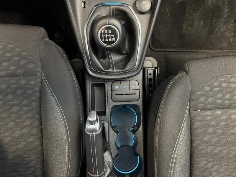 Vue plongeante sur la console centrale intérieure noire du Ford Puma 2023 avec levier de vitesse manuel et porte-gobelets éclairés.