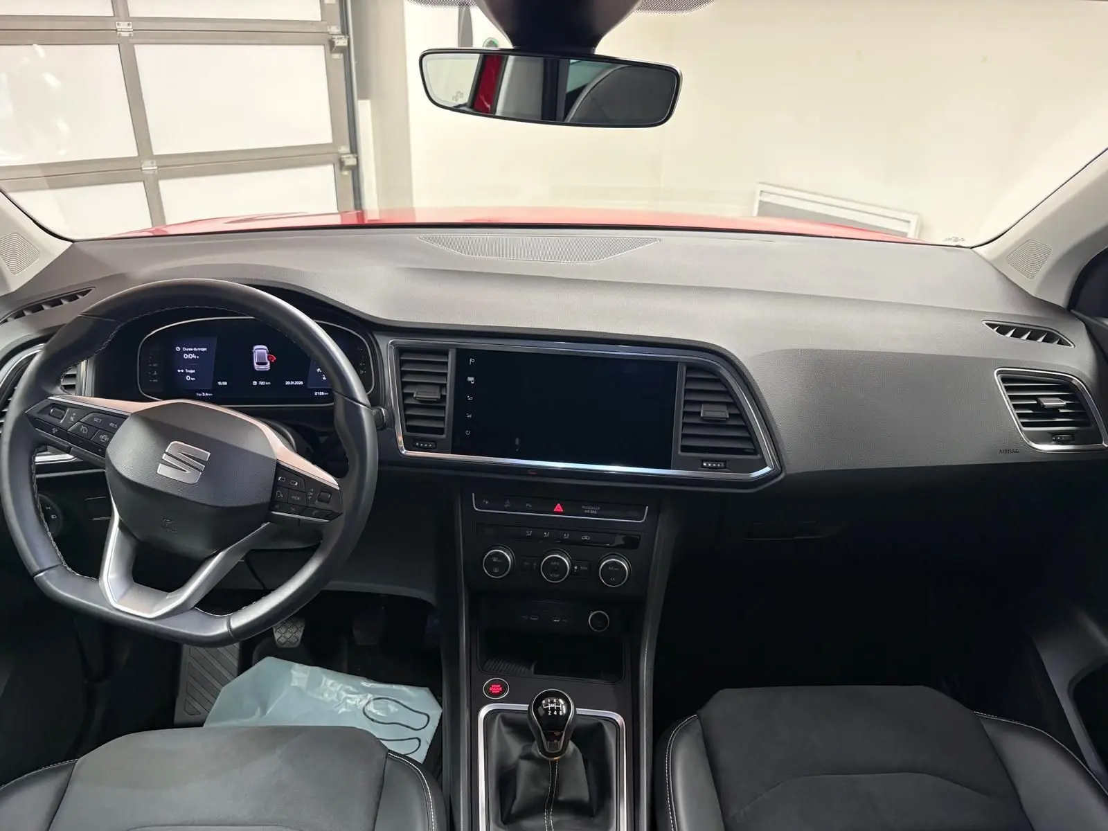 Vue intérieure avant du tableau de bord et volant de la SEAT Ateca 2024 avec boîte manuelle et toit rouge visible par le pare-brise.