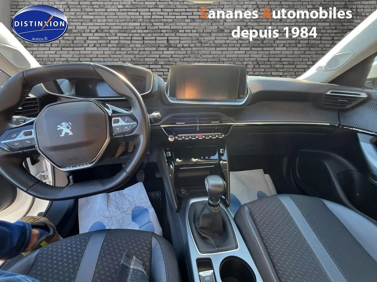 Vue intérieure avant du Peugeot 2008 blanc, mettant en valeur le volant, la console centrale et la sellerie tri-matière.