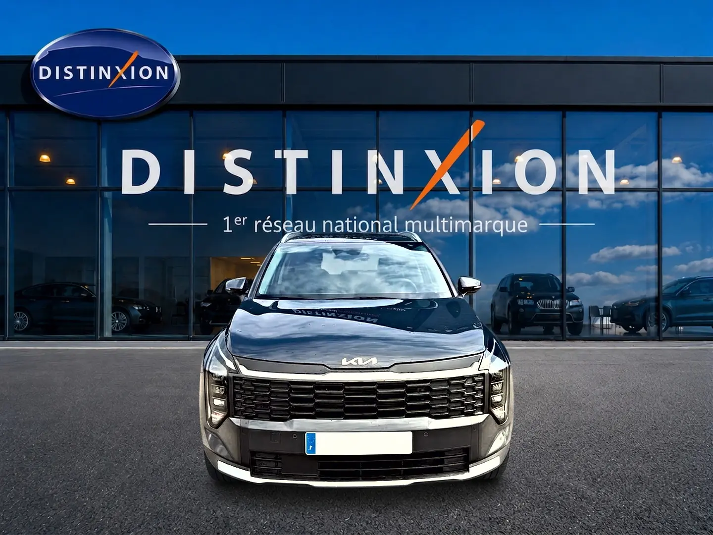 Vue frontale d'un KIA SPORTAGE 1.6 hybride gris eclipse garé devant une vitrine avec logo Distinxion.