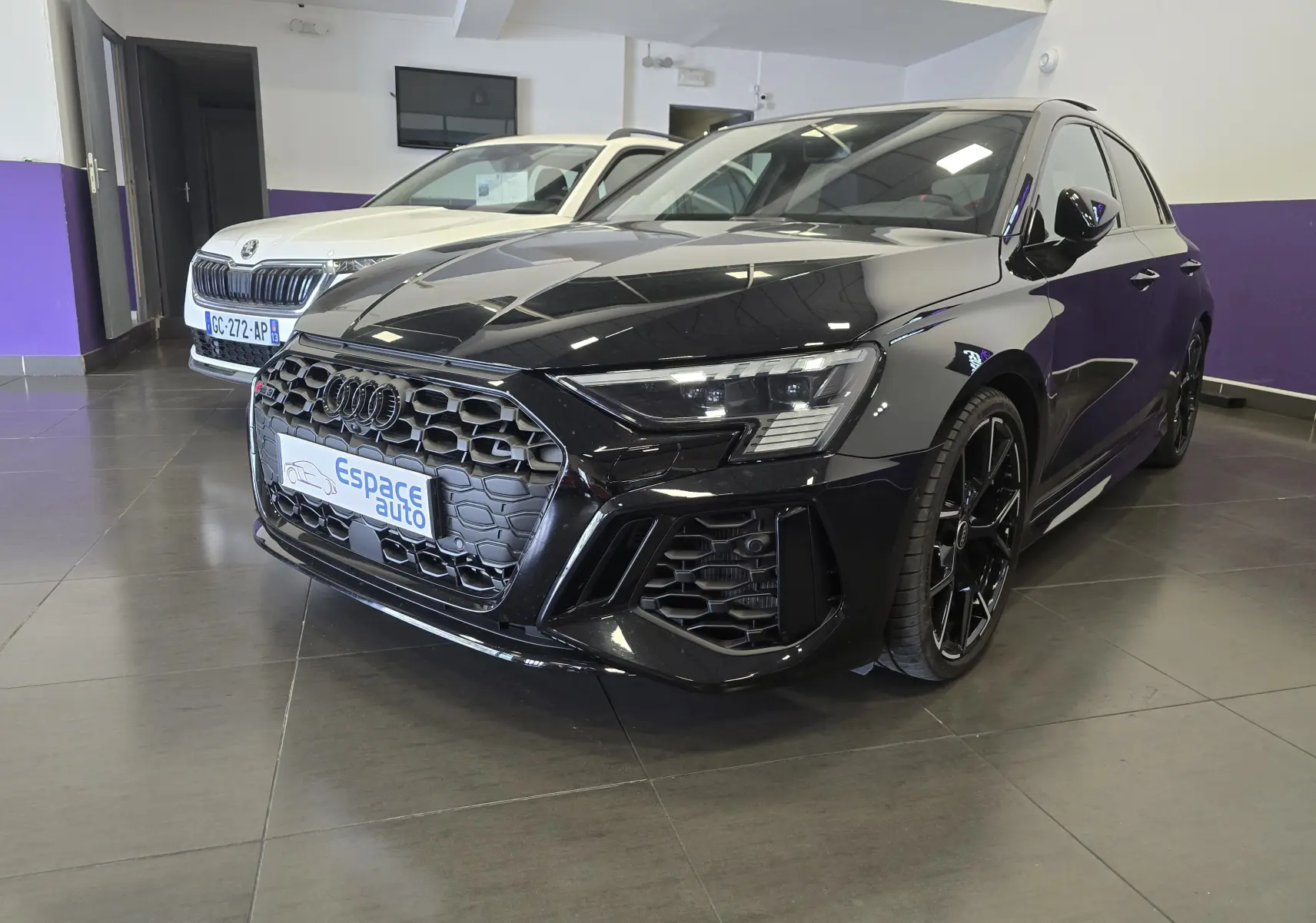 Audi RS3 Sportback noir vue 3/4 avant droit, calandre hexagonale noire et jantes noires en showroom.