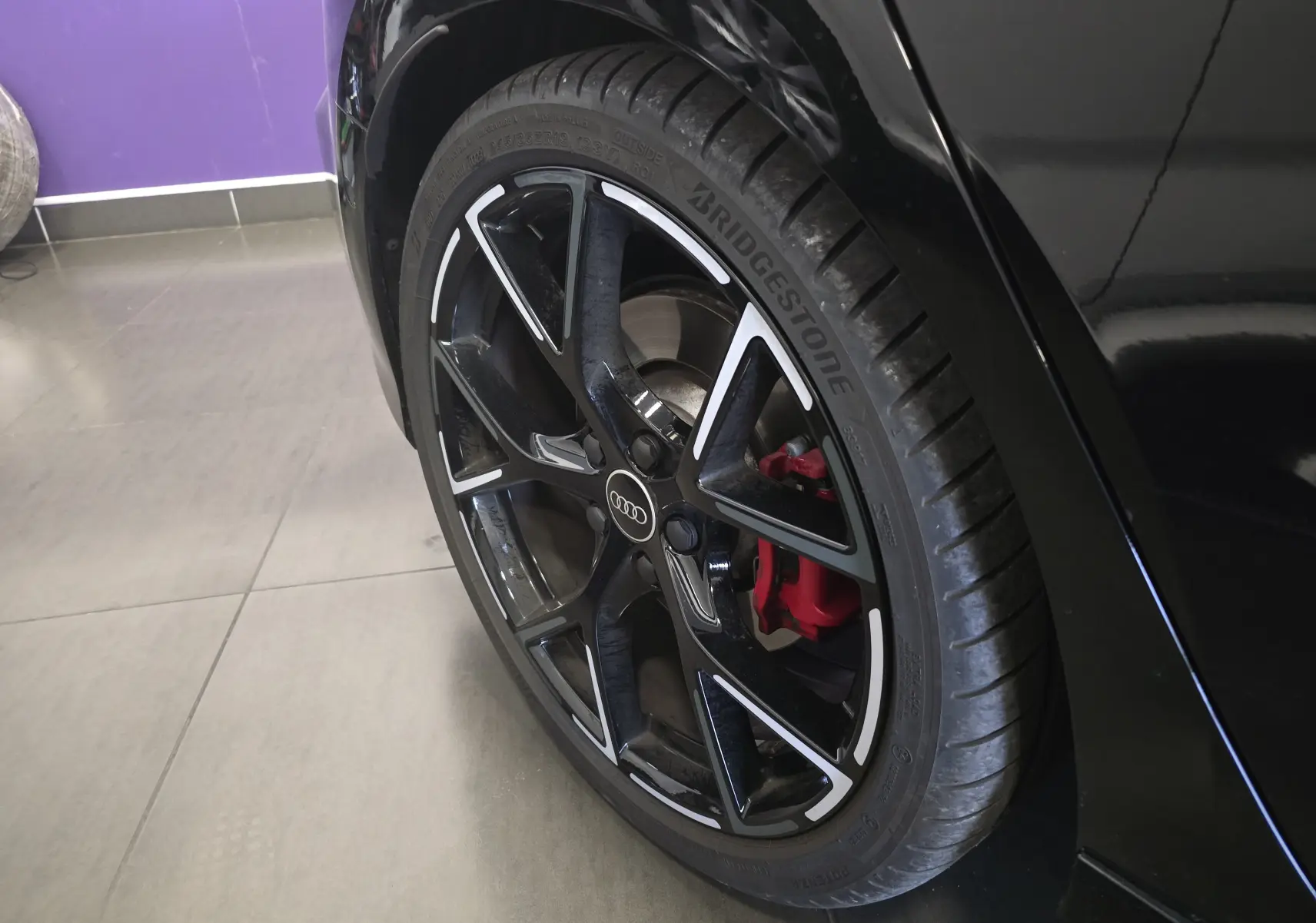 Gros plan sur la roue arrière droite noire d'une Audi RS3 Sportback 2023 avec étrier de frein rouge et jante noire à inserts argentés.