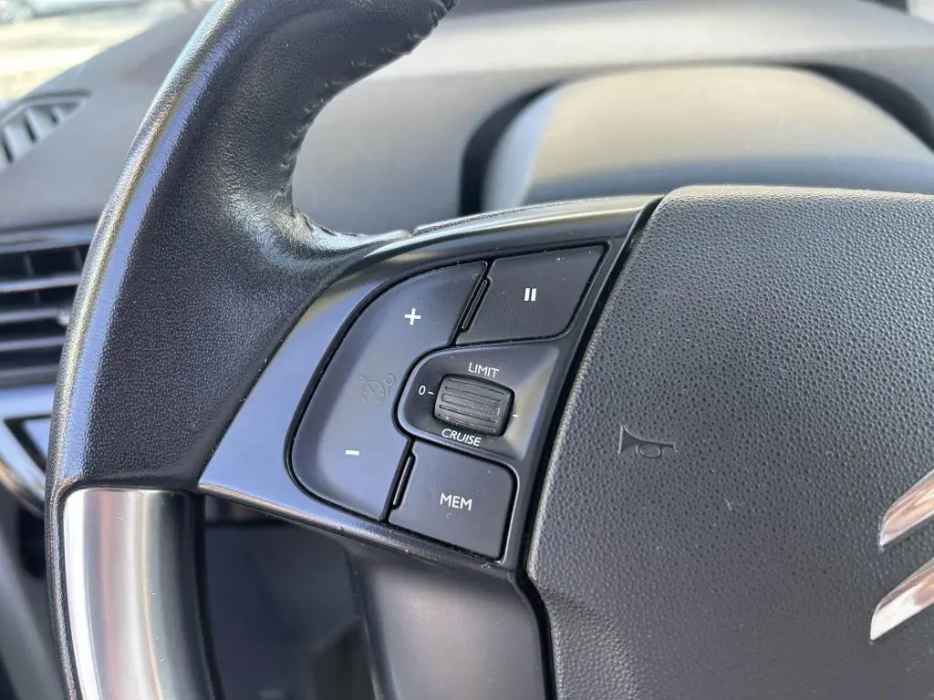 Gros plan sur les commandes de régulateur de vitesse à gauche du volant du Citroën Grand C4 Spacetourer beige clair.