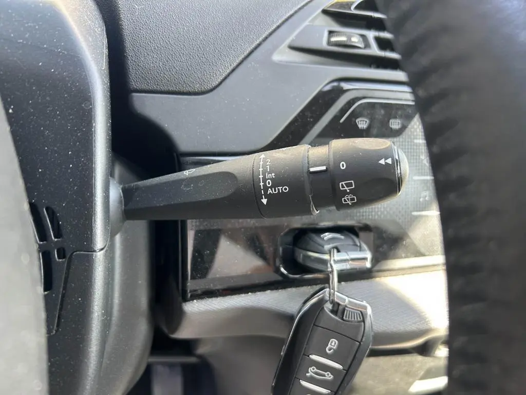 Gros plan sur la commande d'essuie-glace noire à gauche du volant dans l'habitacle sombre du Citroën Grand C4 Spacetourer.
