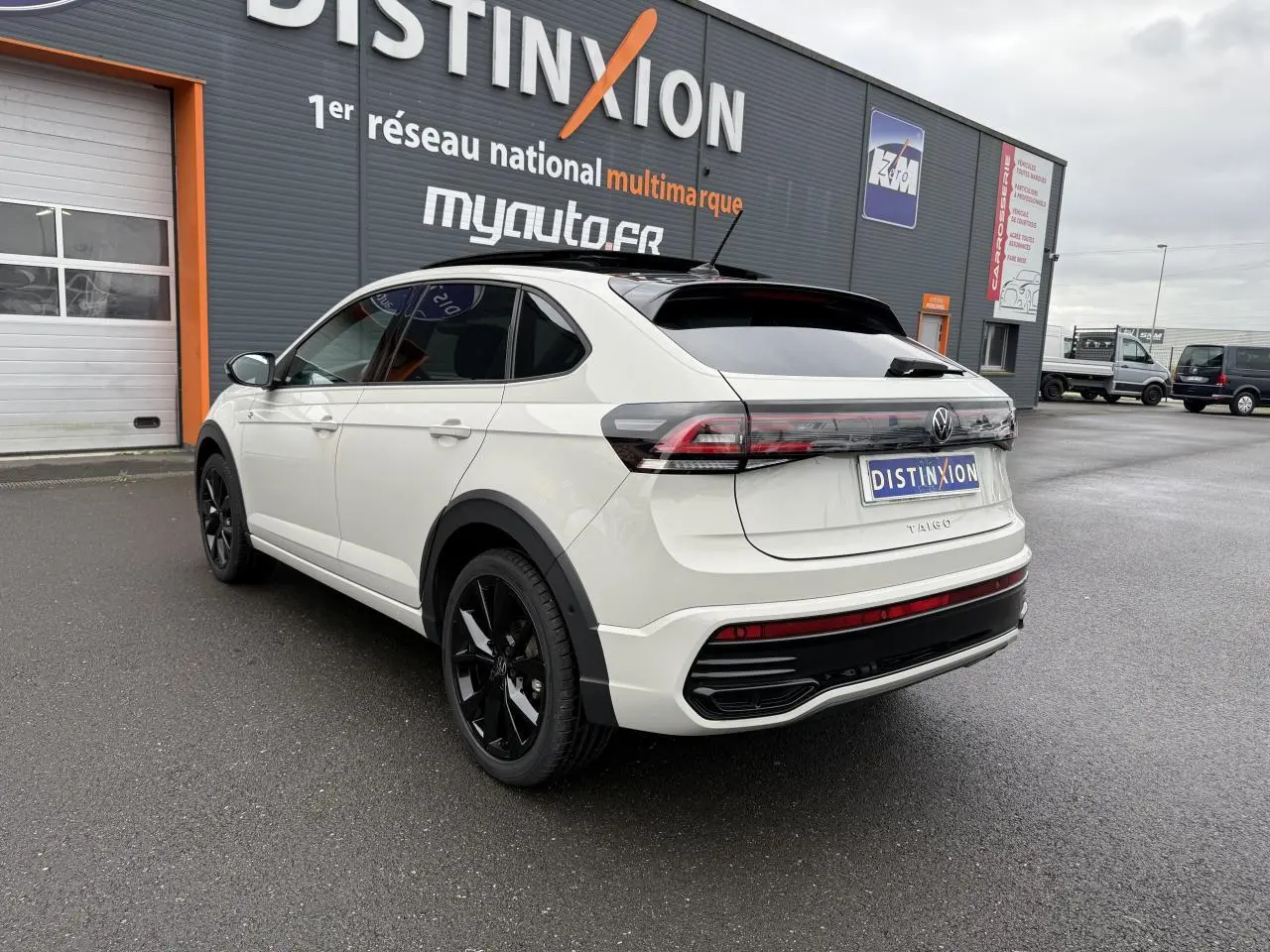 Vue 3/4 arrière droite d'un Volkswagen Taigo blanc avec jantes noires et vitres teintées sur parking.