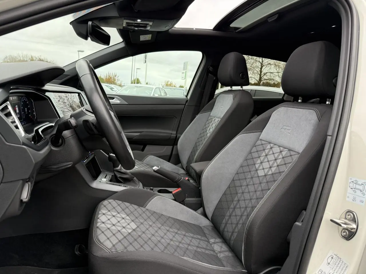 Vue intérieure côté gauche du Volkswagen Taigo 2024 avec sièges avant R-Line en tissu gris et toit ouvrant panoramique.