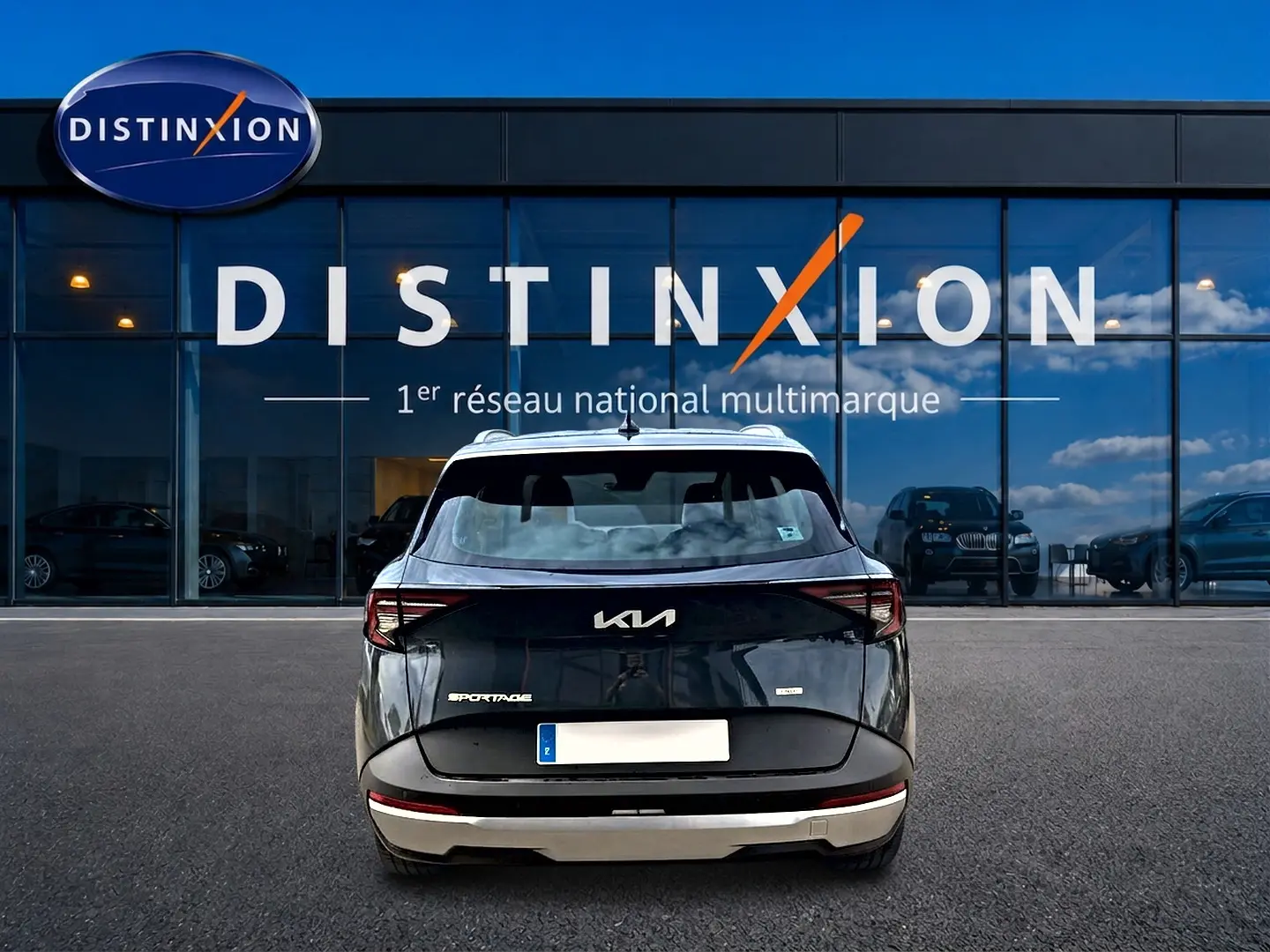 Vue arrière d'un KIA Sportage gris eclipse 2026 garé devant une vitrine avec logo Distinxion.