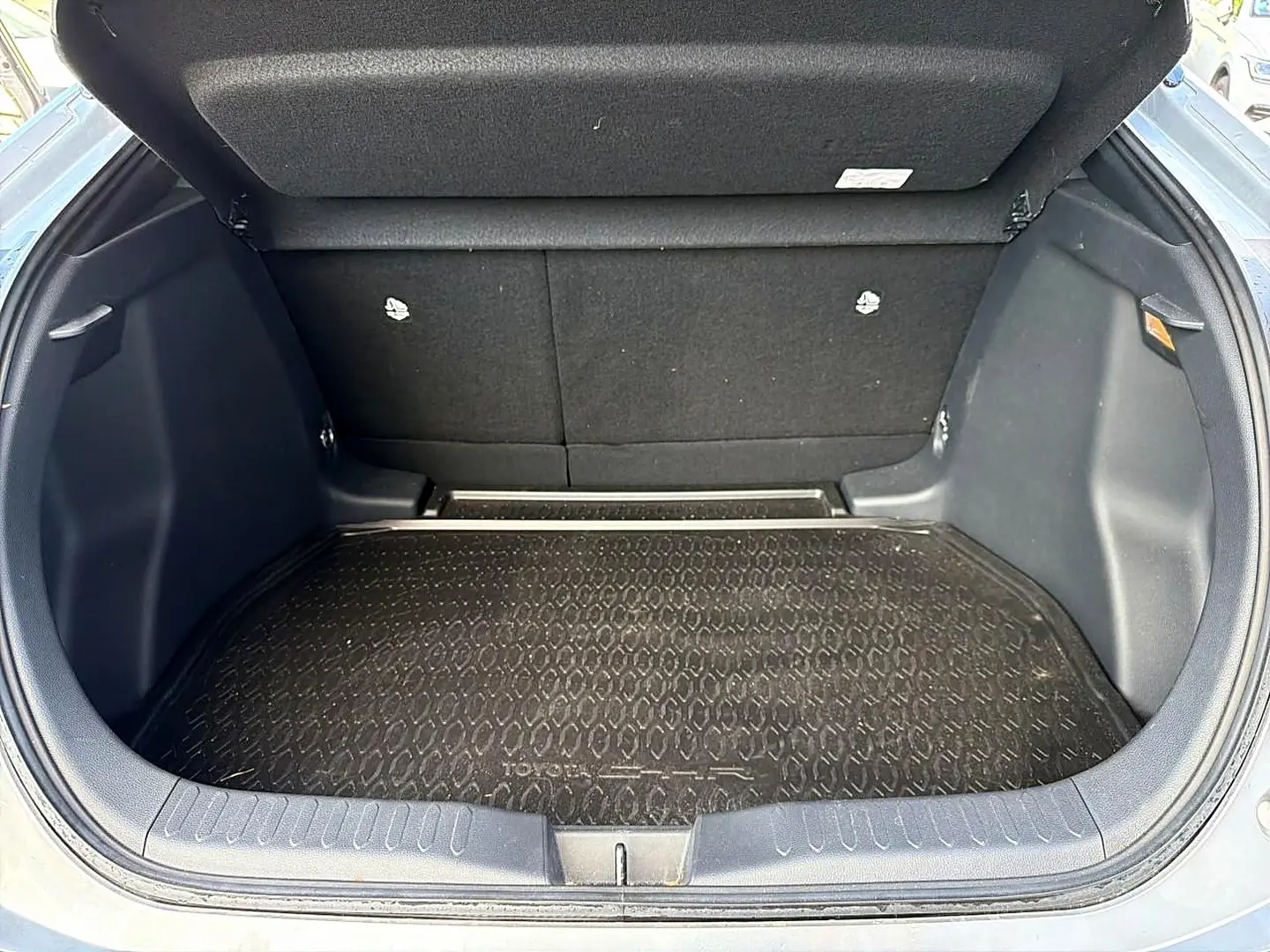 Coffre ouvert vu de face d’un Toyota C-HR gris, avec tapis de coffre noir texturé et banquette arrière rabattable.