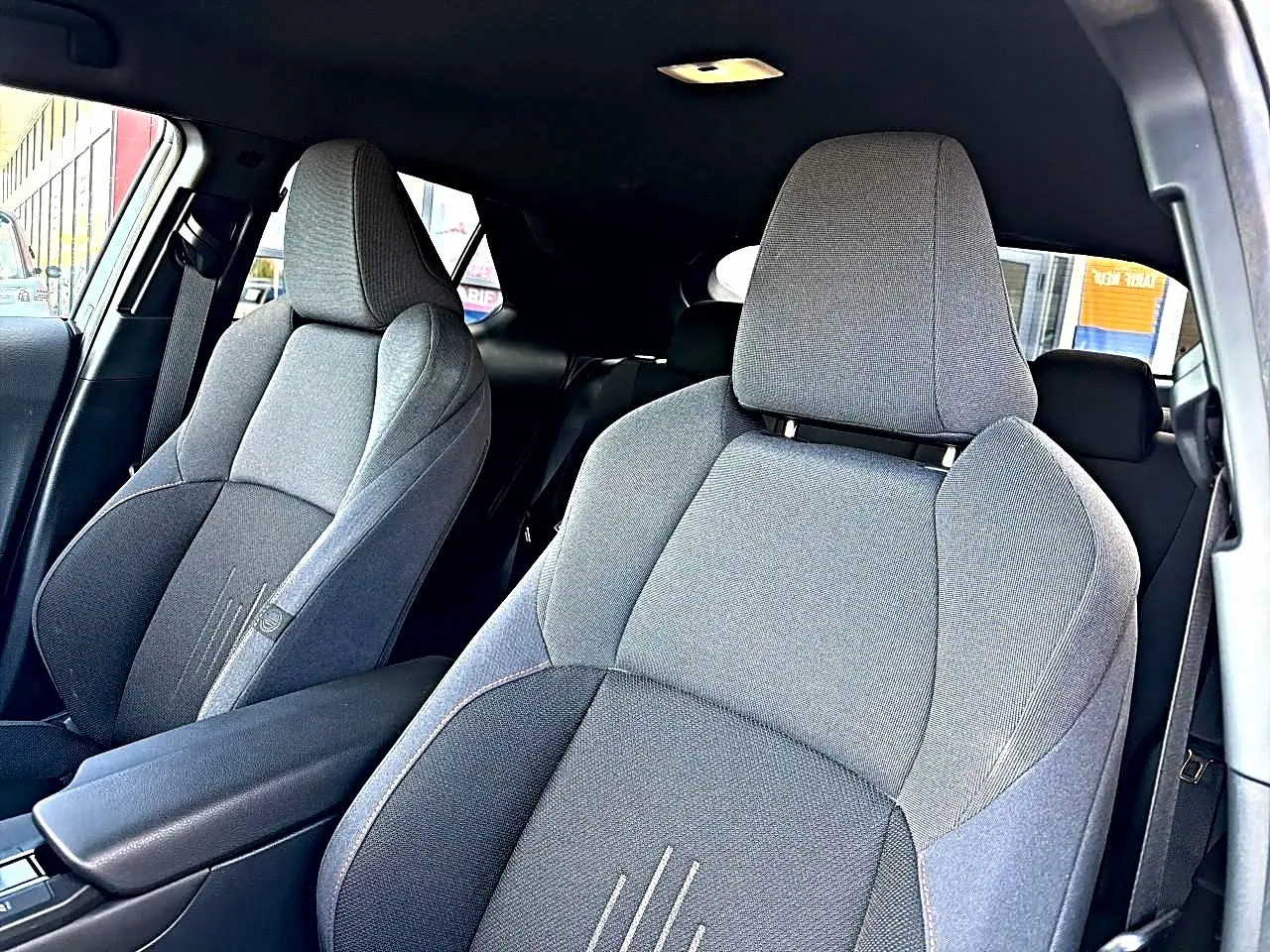 Vue intérieure des sièges avant gris foncé du Toyota C-HR 1.8 hybride 2025 avec accoudoir central et ceintures visibles.