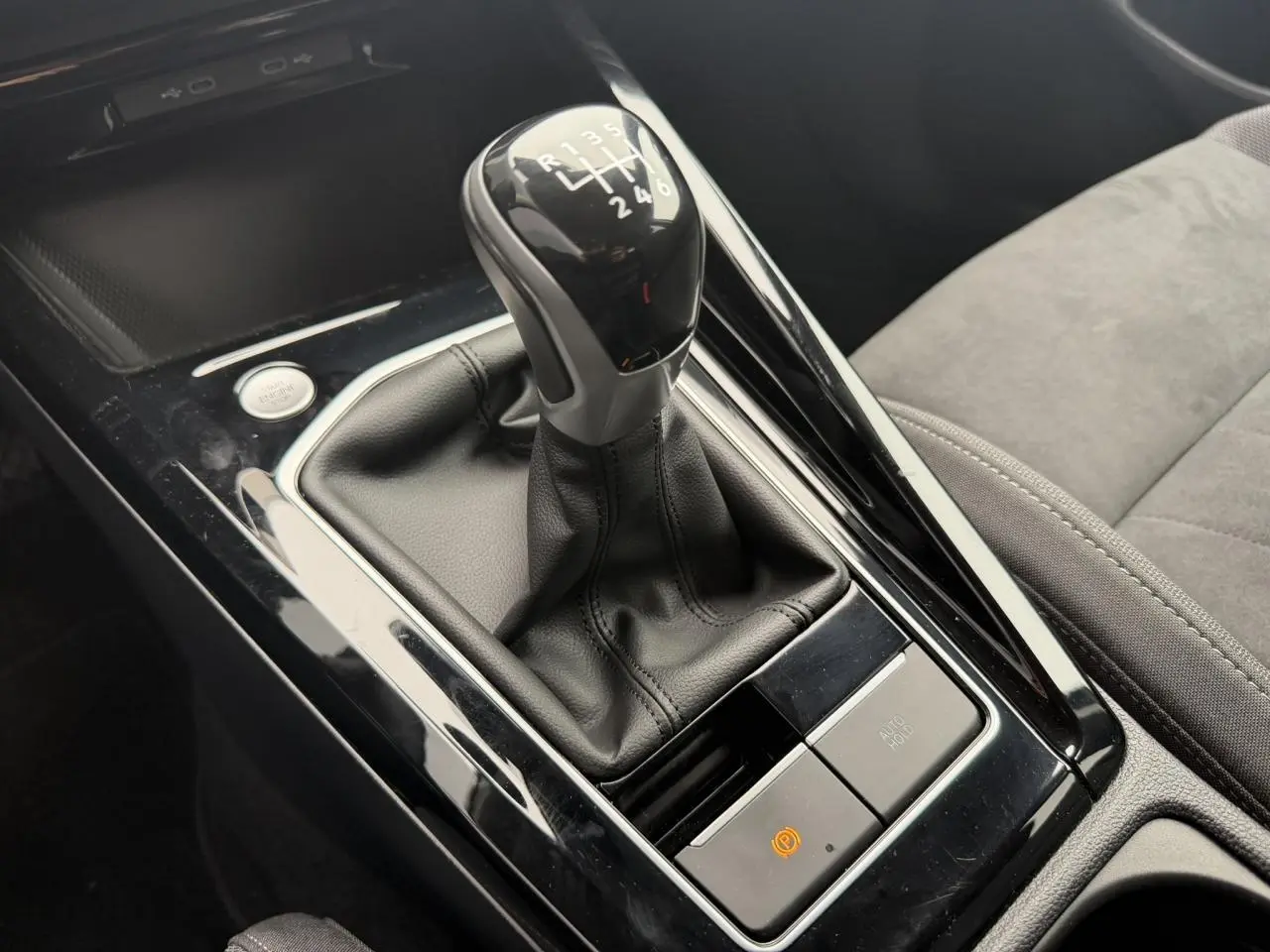 Gros plan sur le levier de vitesse manuel noir et cuir de la Volkswagen Golf VIII 1.5 TSI, avec console brillante autour.