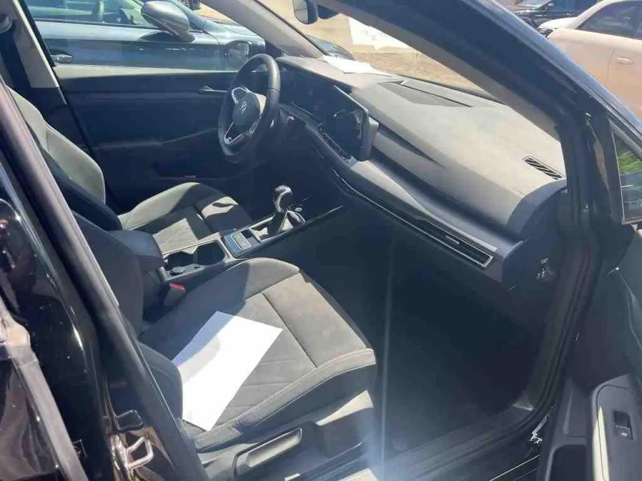 Vue intérieure côté conducteur d'une Volkswagen Golf VIII 1.5 TSI noire avec sellerie microfleece et tableau de bord moderne.