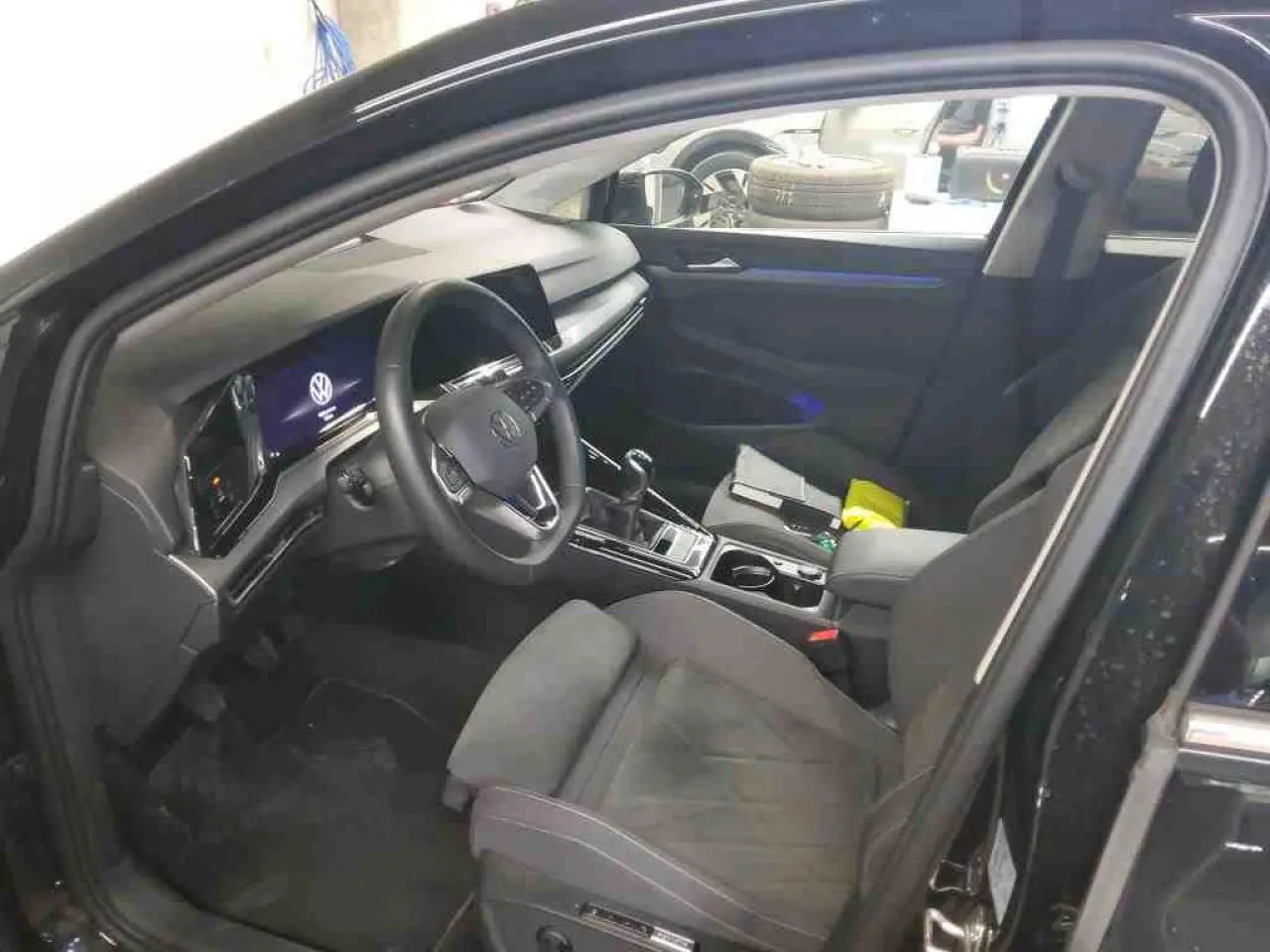 Vue intérieure côté conducteur de la Volkswagen Golf VIII Deep Black avec tableau de bord digital et sellerie microfleece noire.