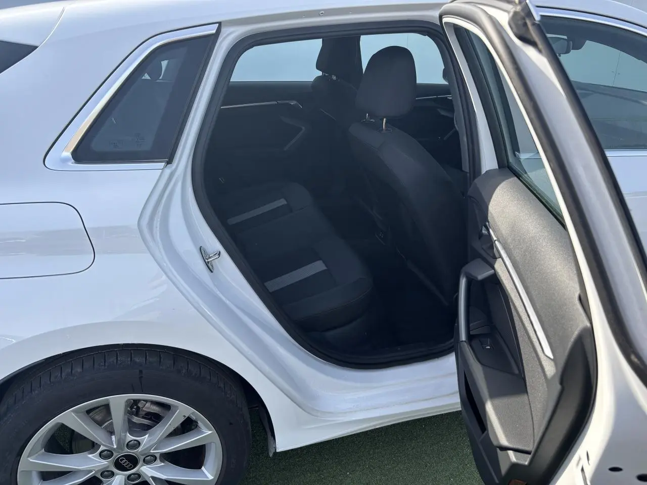 Vue côté gauche arrière d'une Audi A3 Sportback 2024 blanc Arkona avec porte arrière ouverte et intérieur noir visible.