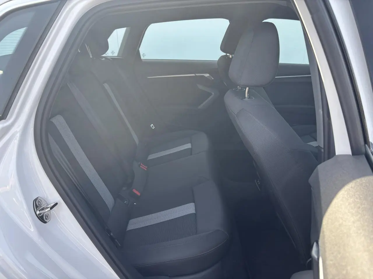Vue intérieure côté gauche de l'Audi A3 Sportback 2024 en Blanc Arkona, sièges tissu noir avec bandes grises.