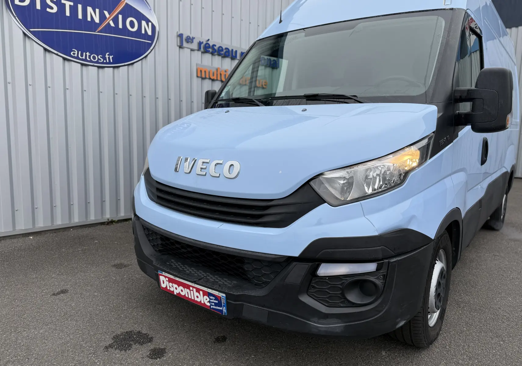 Vue 3/4 avant droit d’un Iveco Daily Fourgon bleu clair de 2017 avec calandre noire et phares allumés.