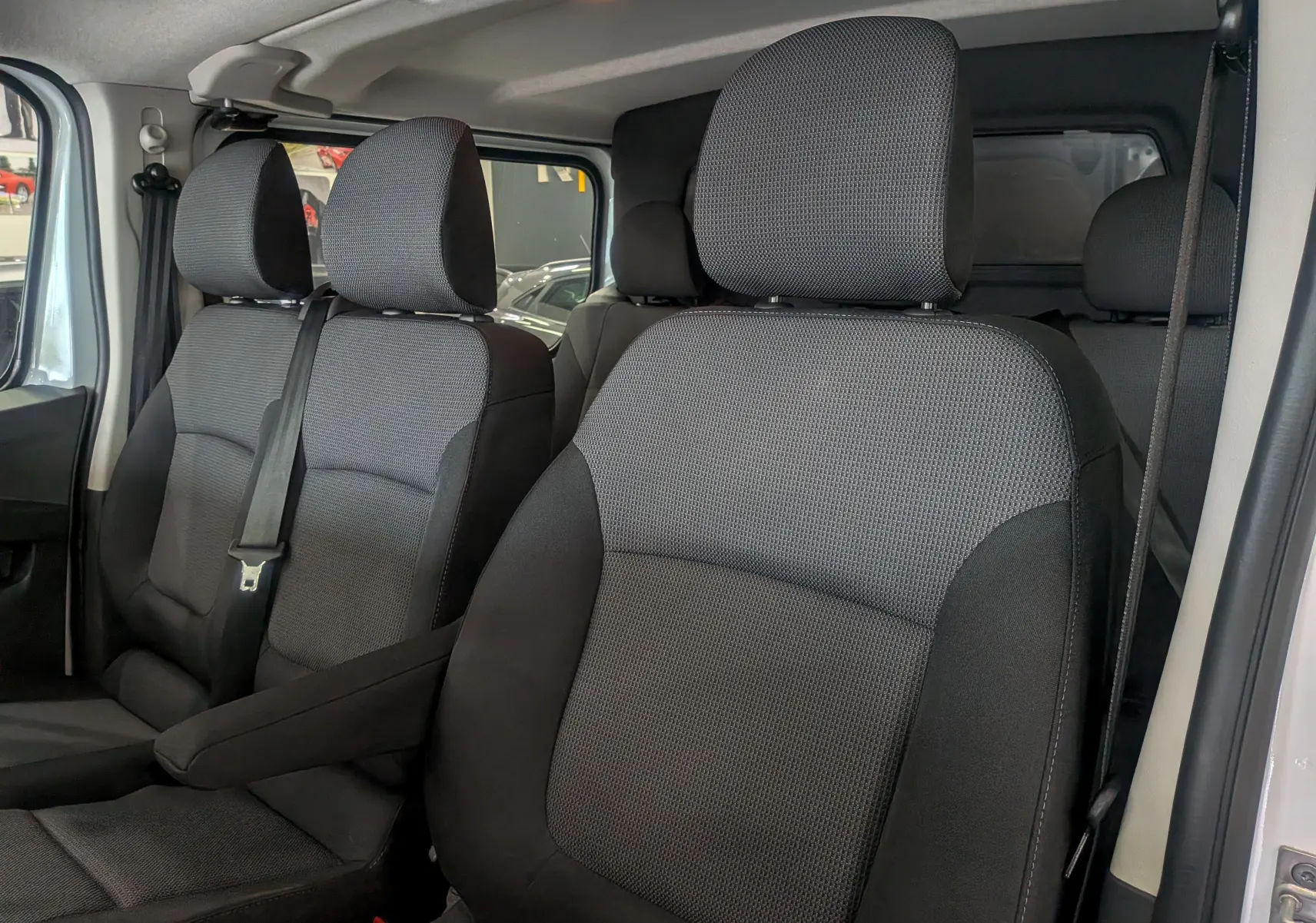Vue intérieure rapprochée des sièges avant en tissu gris foncé du Renault Trafic Cabine Approfondie blanc minéral 2023.