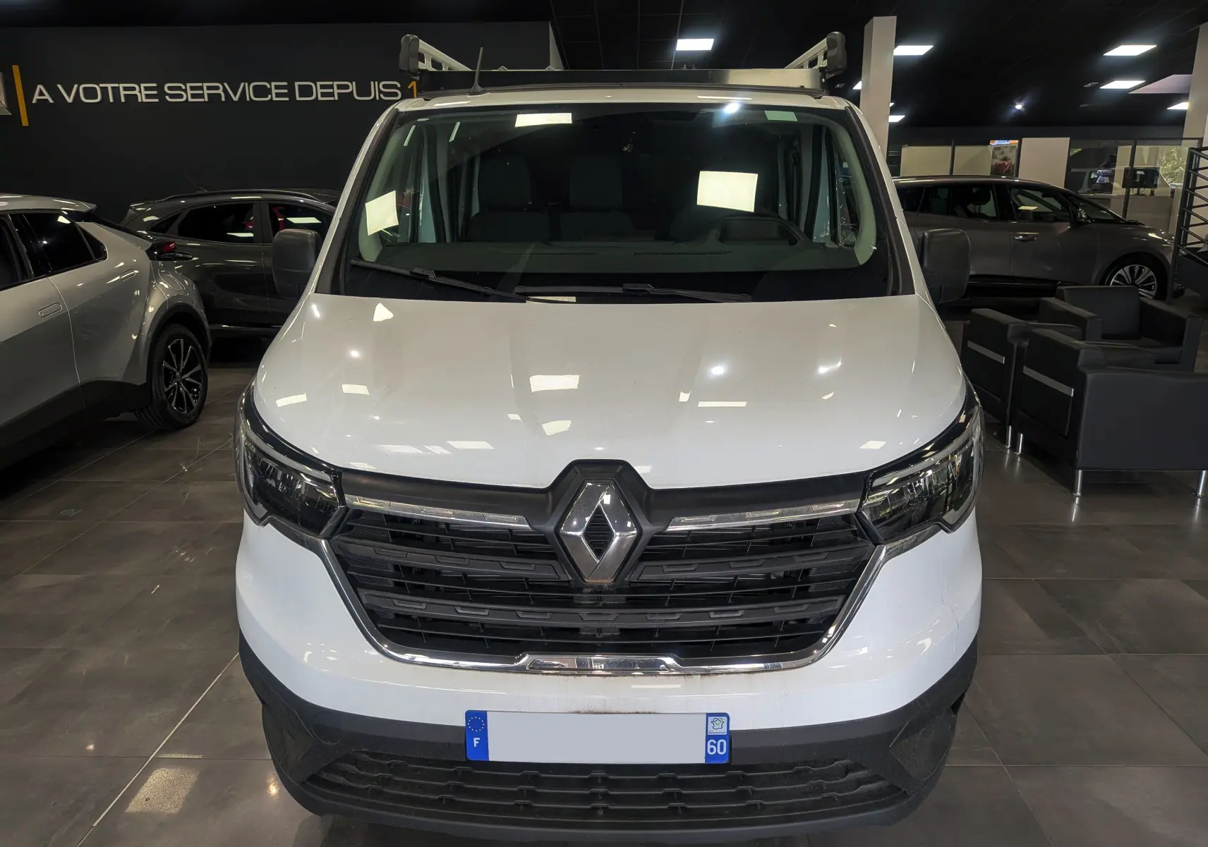 Vue frontale d'un Renault Trafic Cabine Approfondie blanc minéral 2023 en showroom, avec calandre noire et logo Renault.