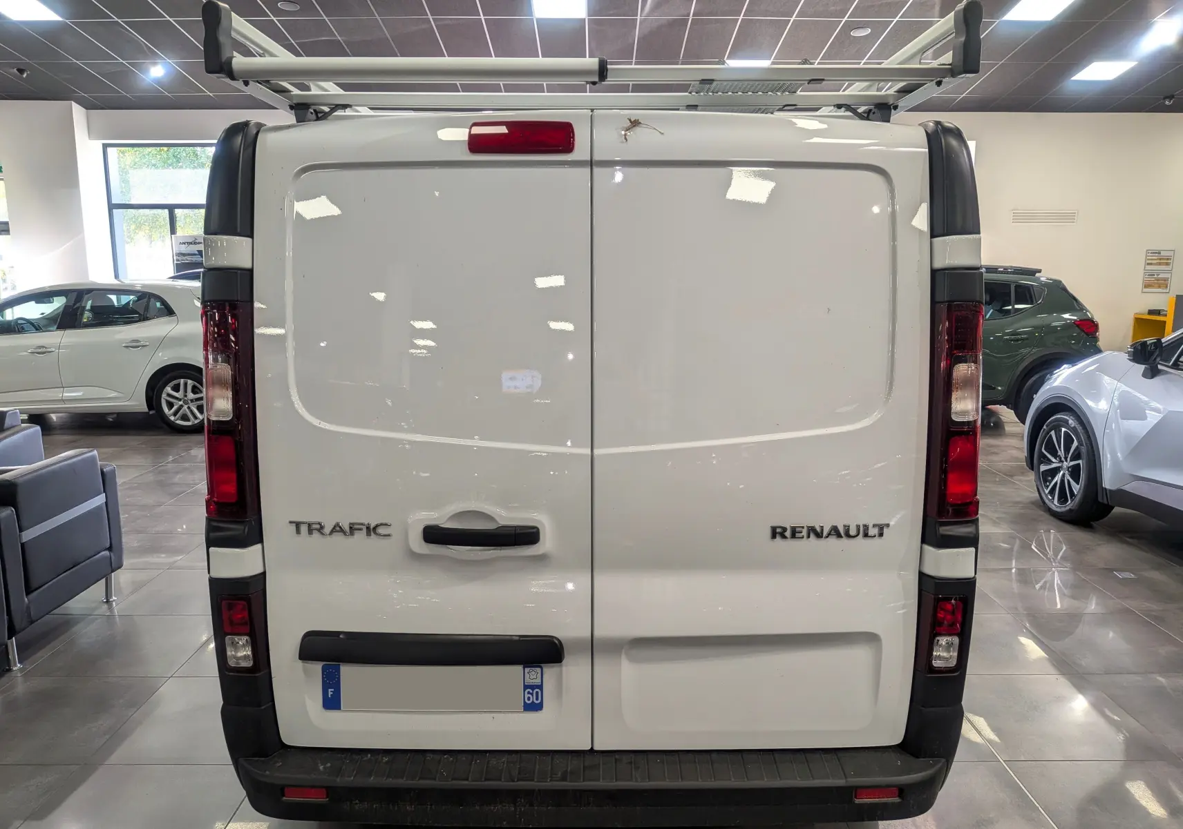 Vue arrière d'un Renault Trafic blanc minéral avec porte double et galerie de toit en intérieur showroom.