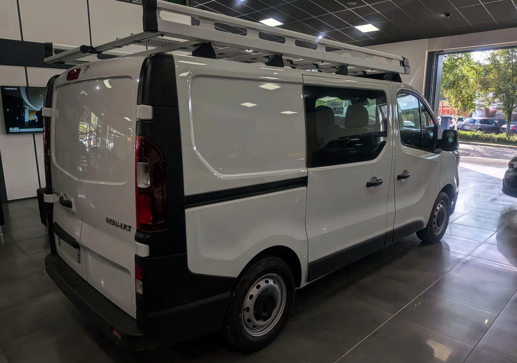 Renault Trafic Cabine Approfondie blanc minéral vu en 3/4 arrière droit avec galerie de toit en intérieur showroom.