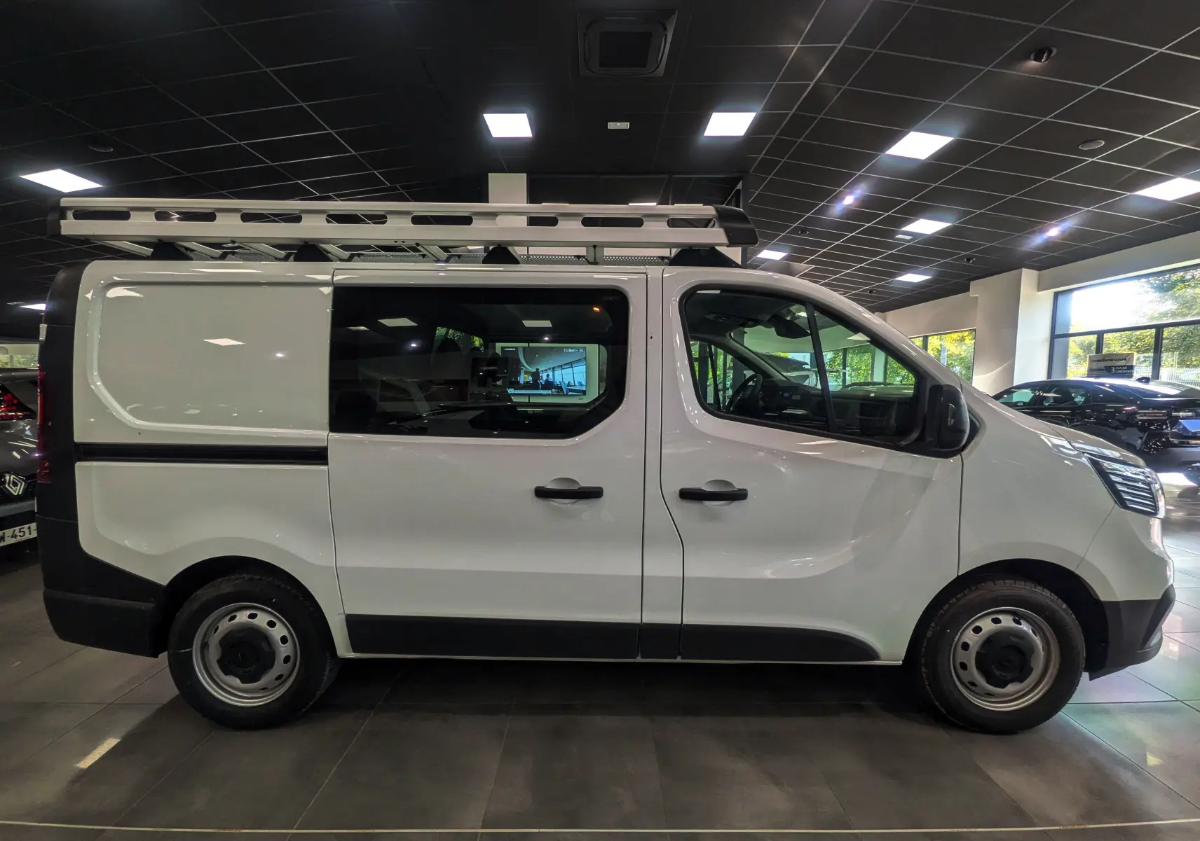 Profil droit du Renault Trafic Cabine Approfondie blanc minéral 2023 avec galerie de toit en intérieur showroom.