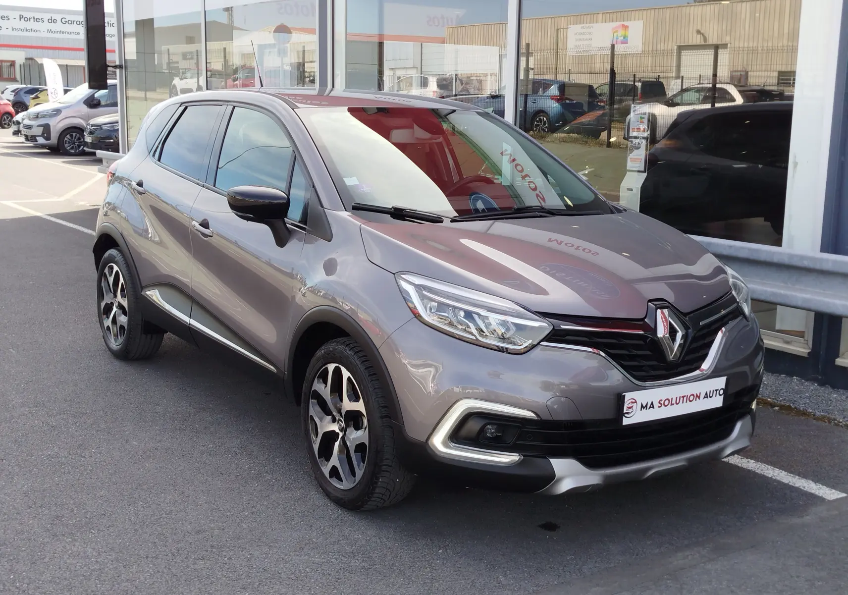 Renault Captur gris Cassiopée en 3/4 avant droit, mettant en valeur ses phares LED et jantes bi-ton.