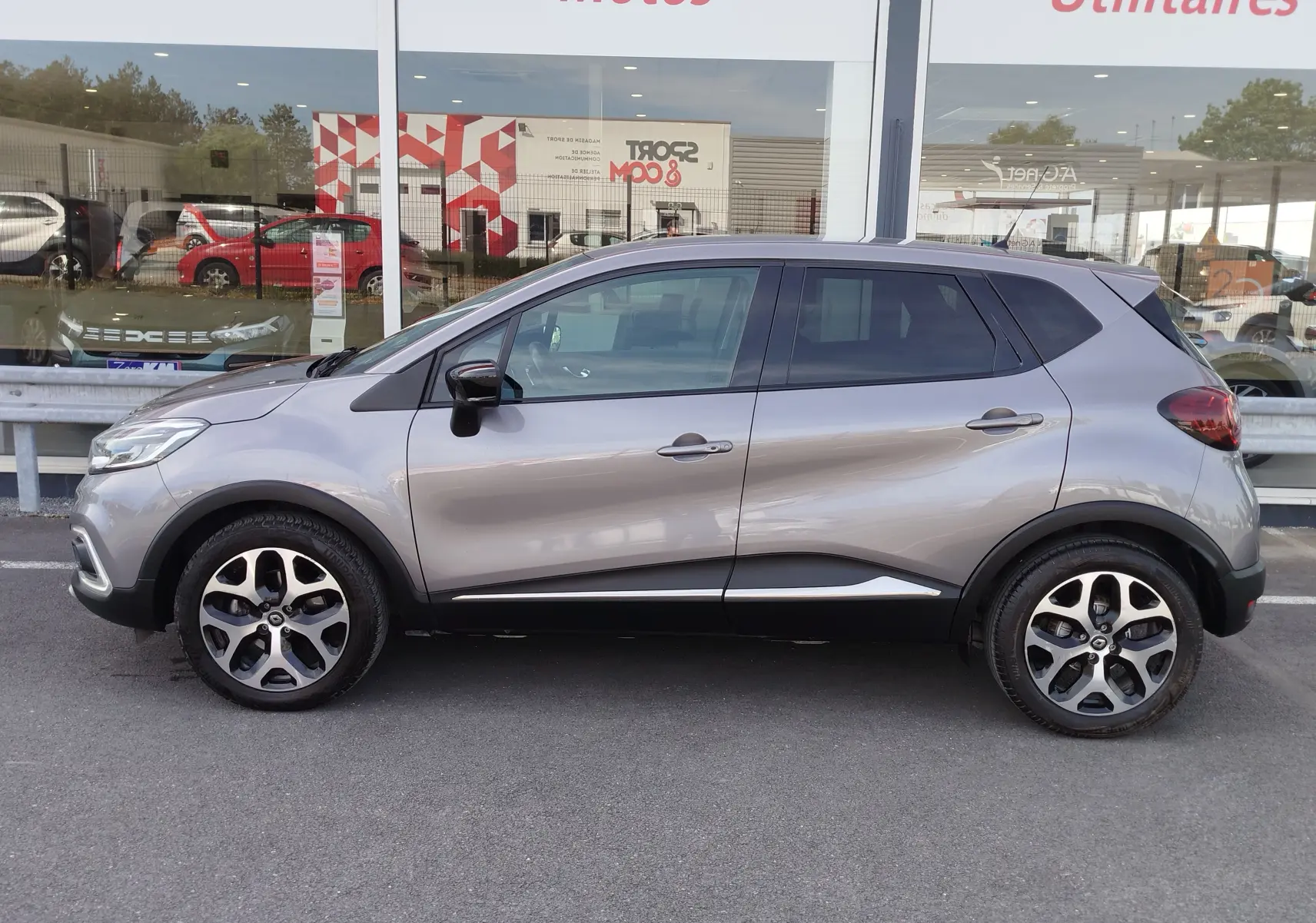 Renault Captur Gris Cassiopée vu de profil côté gauche, avec jantes bi-ton et vitres teintées.
