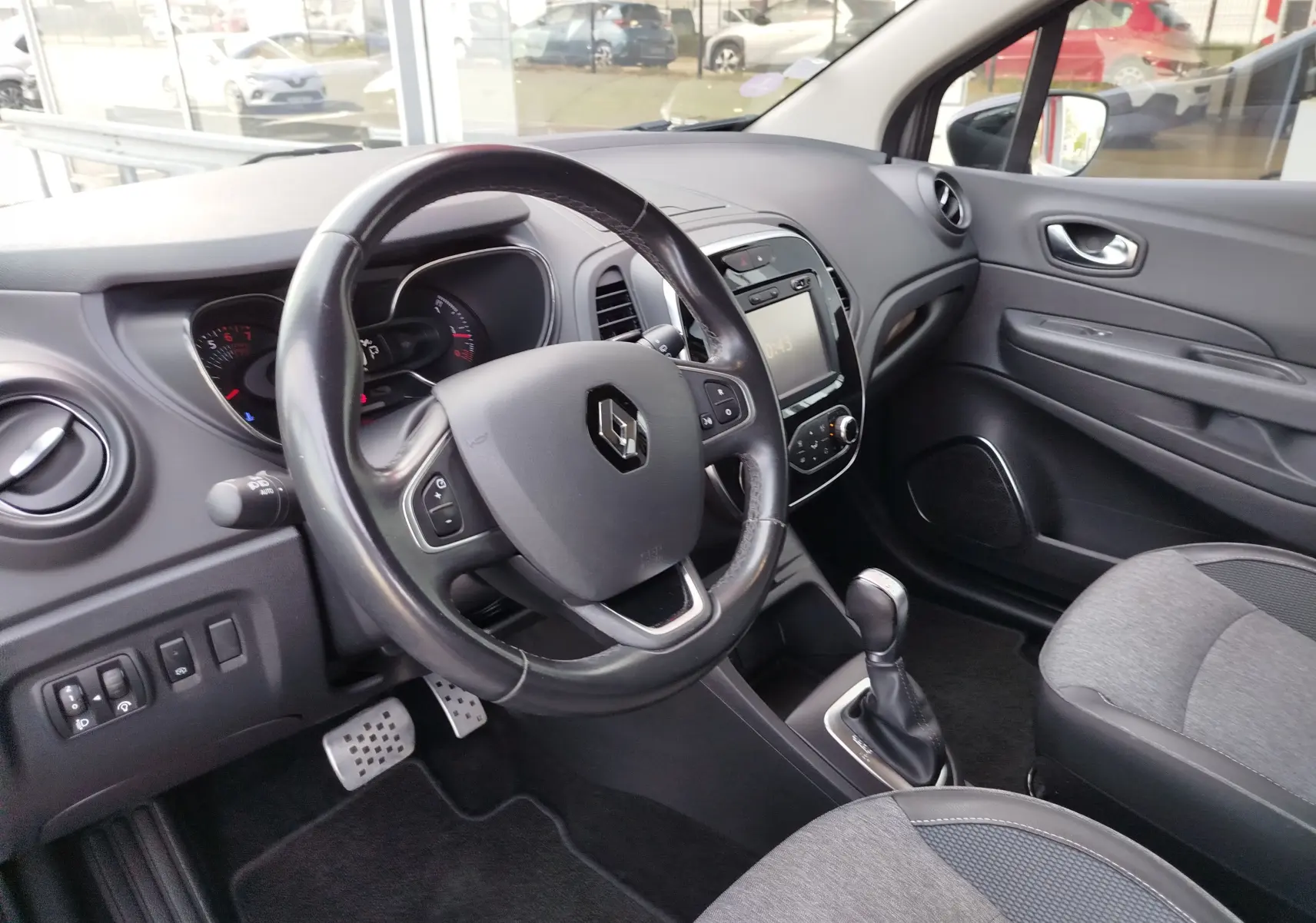 Vue intérieure côté conducteur du Renault Captur gris, avec volant multifonction, écran tactile et levier de boîte automatique.