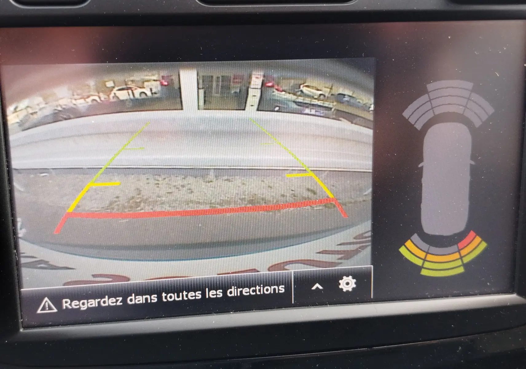 Vue de la caméra de recul du Renault Captur gris Cassiopée, avec lignes de guidage colorées et capteurs d'obstacles affichés.