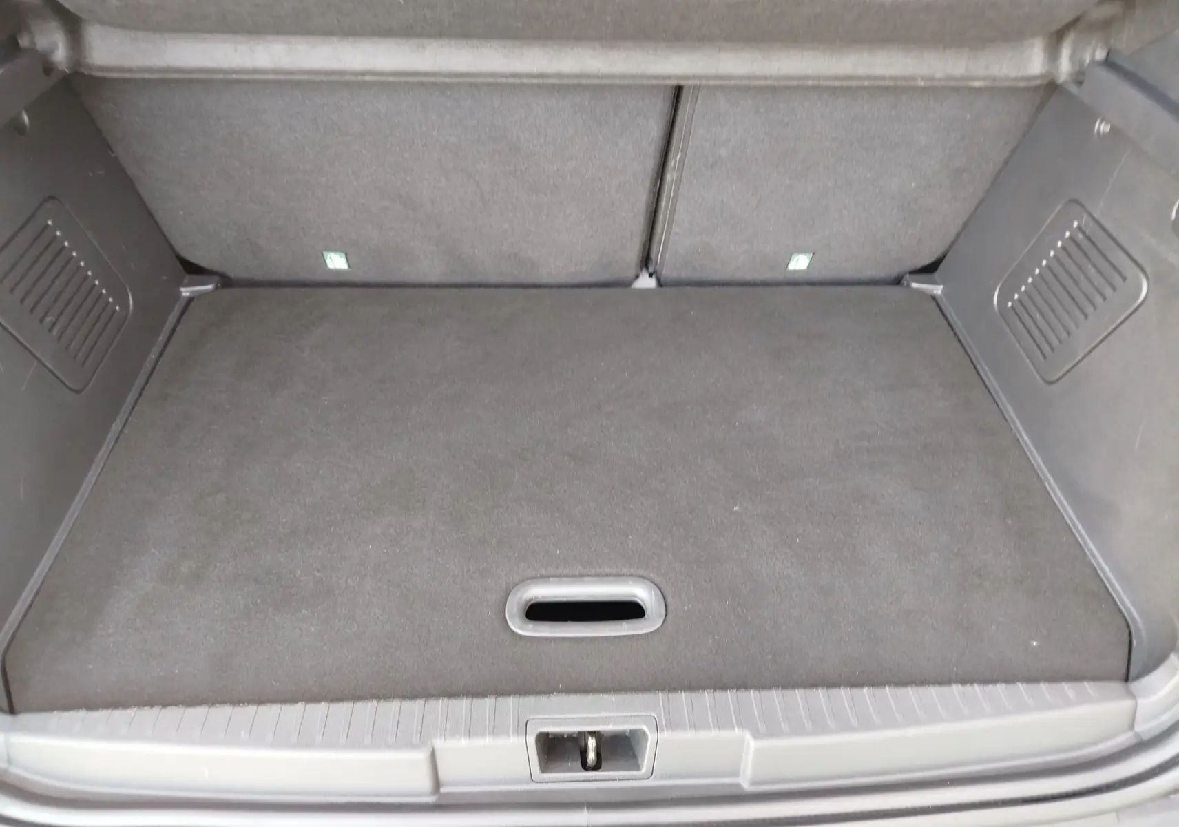 Coffre spacieux et propre du Renault Captur gris Cassiopée, vu de l'arrière avec plancher plat et compartiments latéraux.