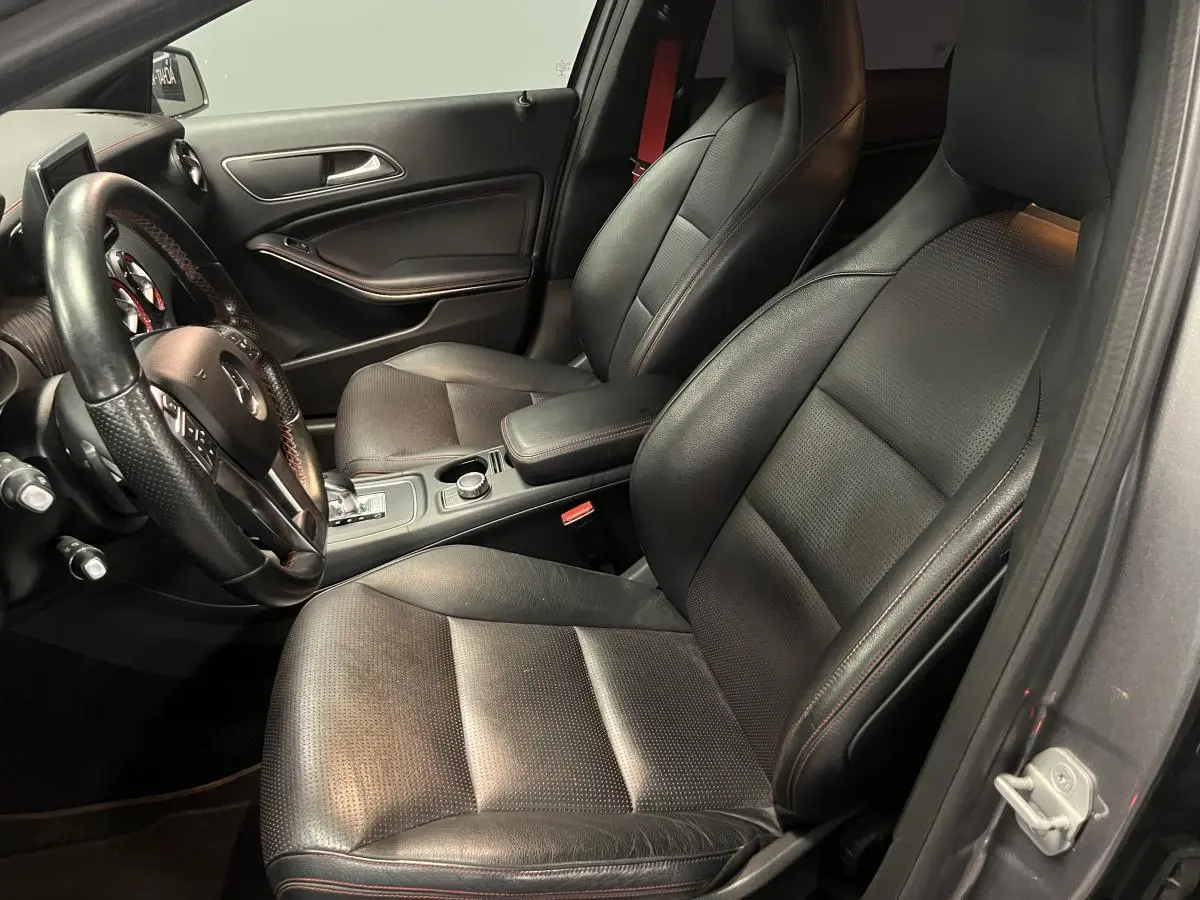 Intérieur avant noir de Mercedes Classe A 45 AMG 2015, sièges sport avec surpiqûres rouges et volant cuir sport.