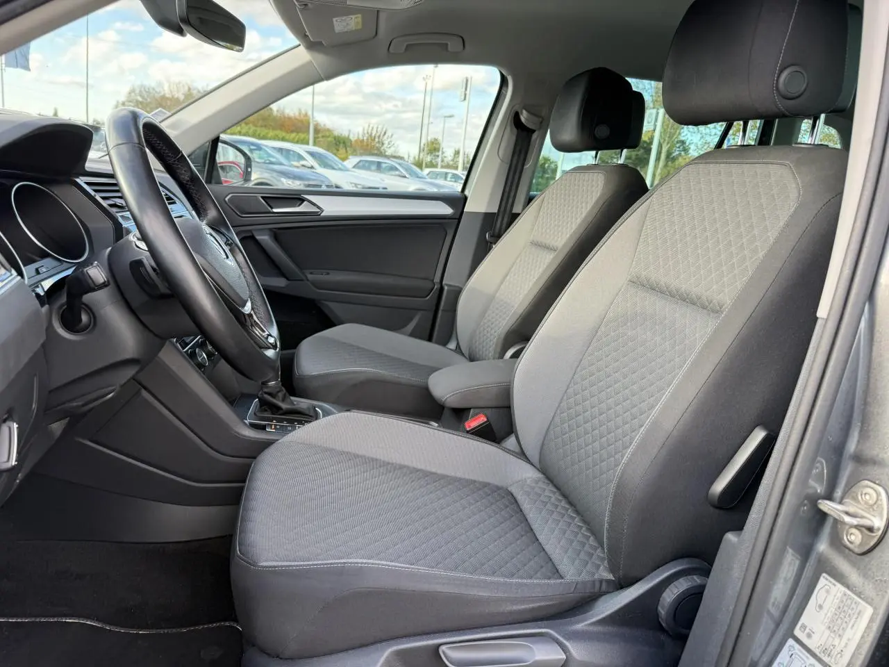 Vue intérieure côté conducteur du Volkswagen Tiguan gris Indium 2018, sièges avant en tissu gris à motif losange.