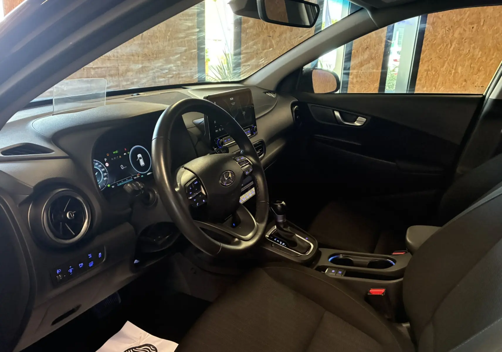 Vue intérieure côté conducteur du Hyundai Kona 2023 noir, montrant le volant multifonction, tableau de bord numérique et console centrale.