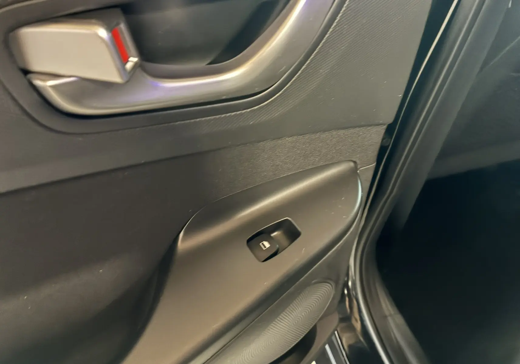 Gros plan sur la poignée intérieure et le bouton de lève-vitre côté gauche d'une Hyundai Kona noire 2023.