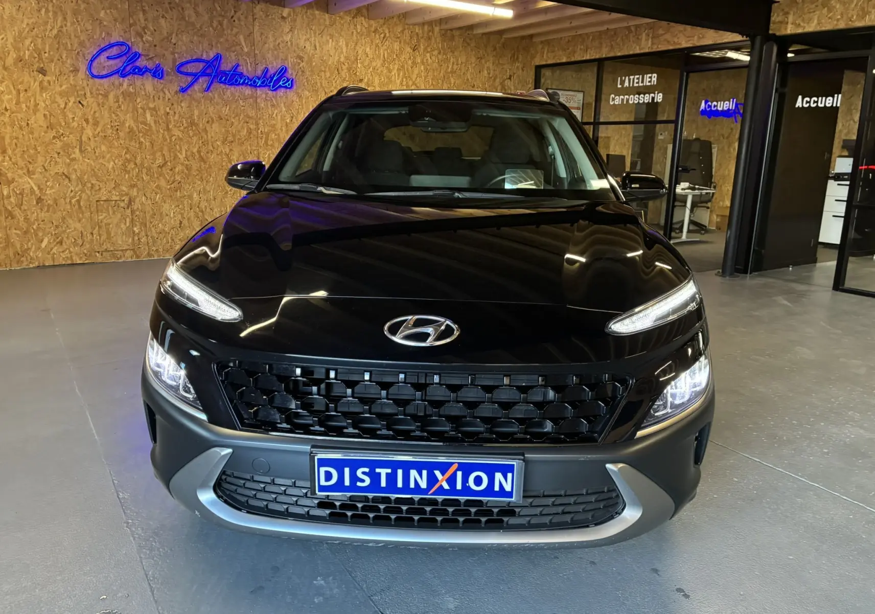 Vue de face d'un Hyundai Kona noir 2023 avec calandre noire et phares allumés dans un showroom.