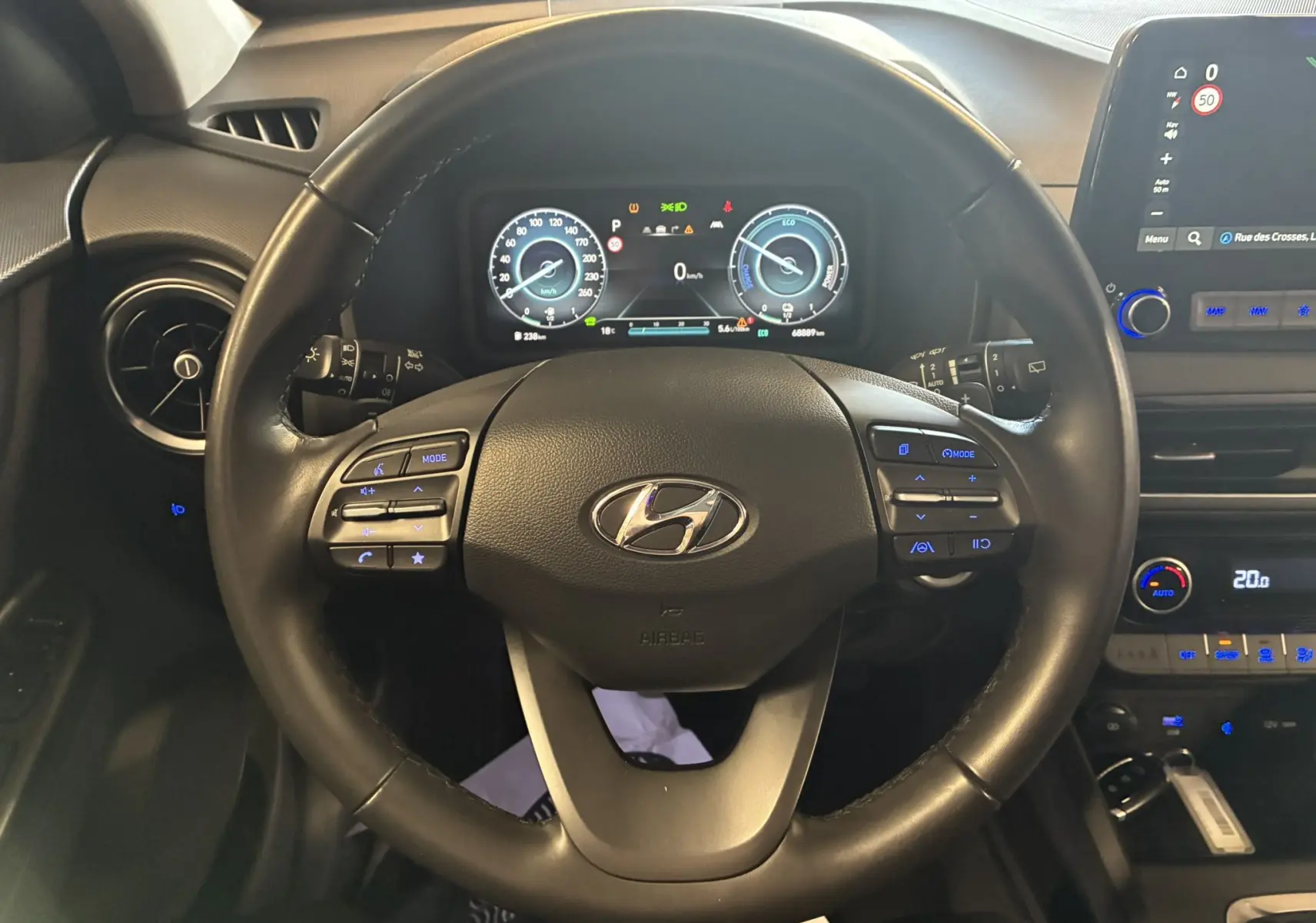 Vue intérieure centrée sur le volant noir du Hyundai Kona 2023, avec tableau de bord numérique et commandes au volant éclairées.