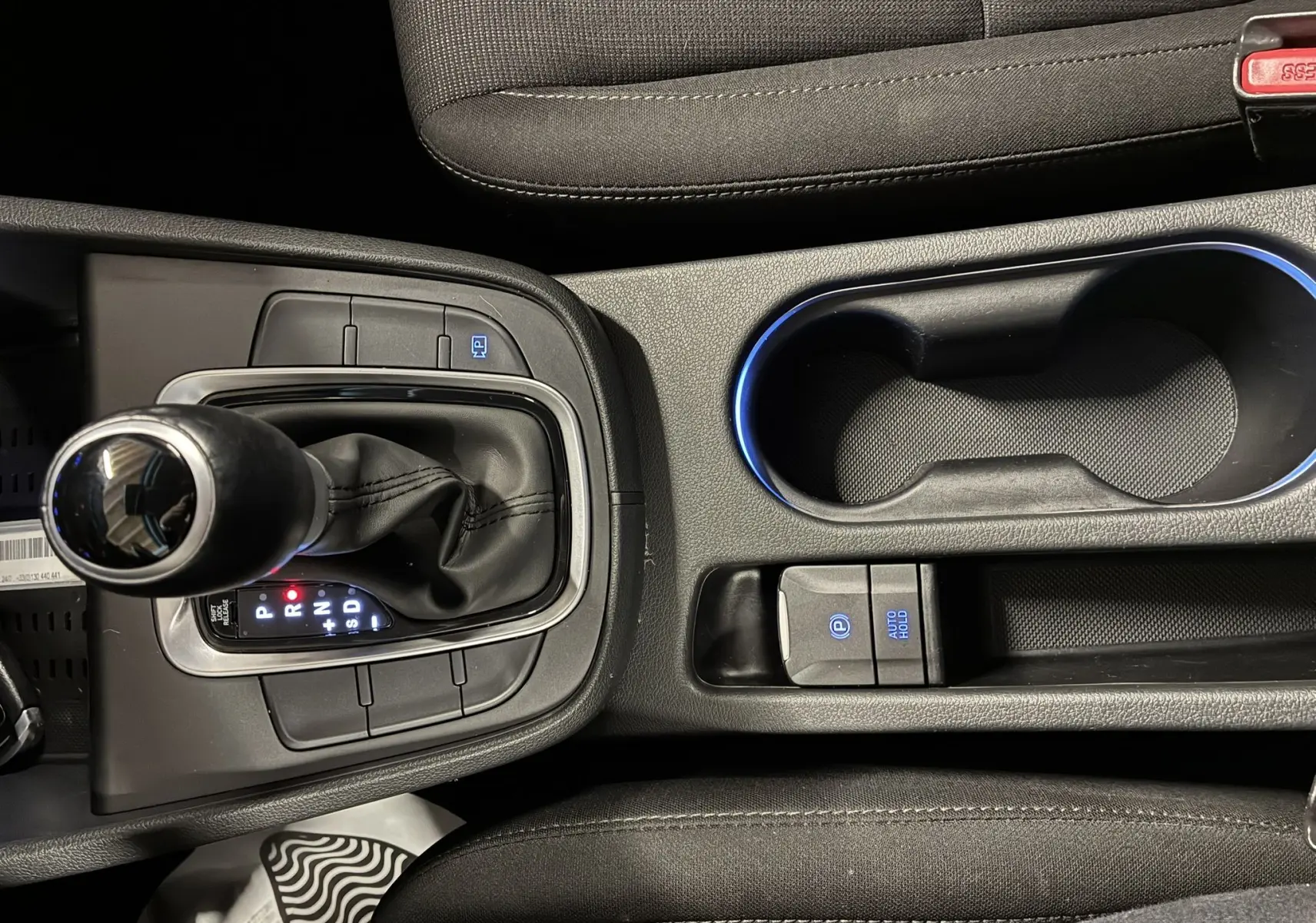 Vue plongeante sur la console centrale noire du Hyundai Kona 2023, mettant en valeur le levier de vitesses automatique et les commandes éclairées.