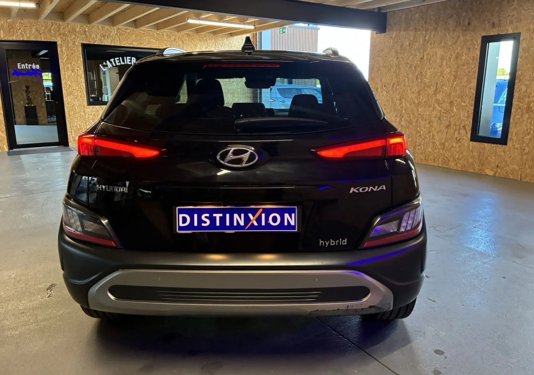 Vue arrière d'un Hyundai Kona noir hybride 2023 avec feux arrière allumés dans un garage éclairé.