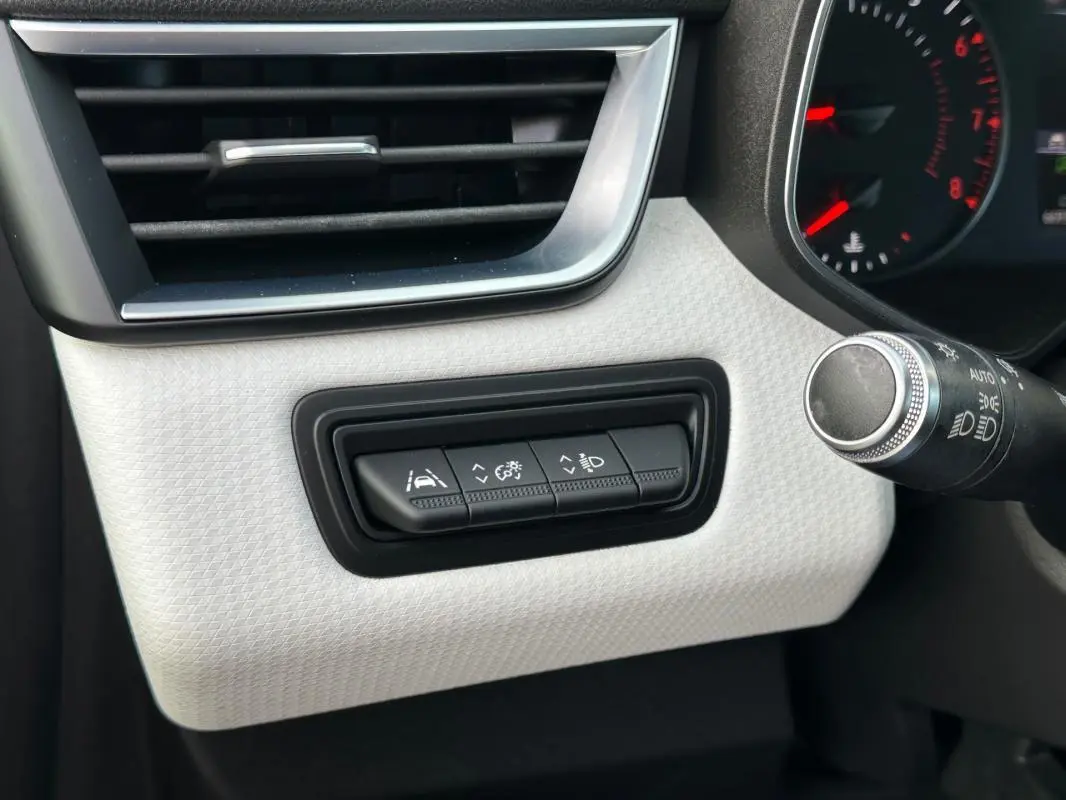 Gros plan sur les commandes d'aide à la conduite à gauche du volant dans l'habitacle clair d'une Renault Clio noire 2021.