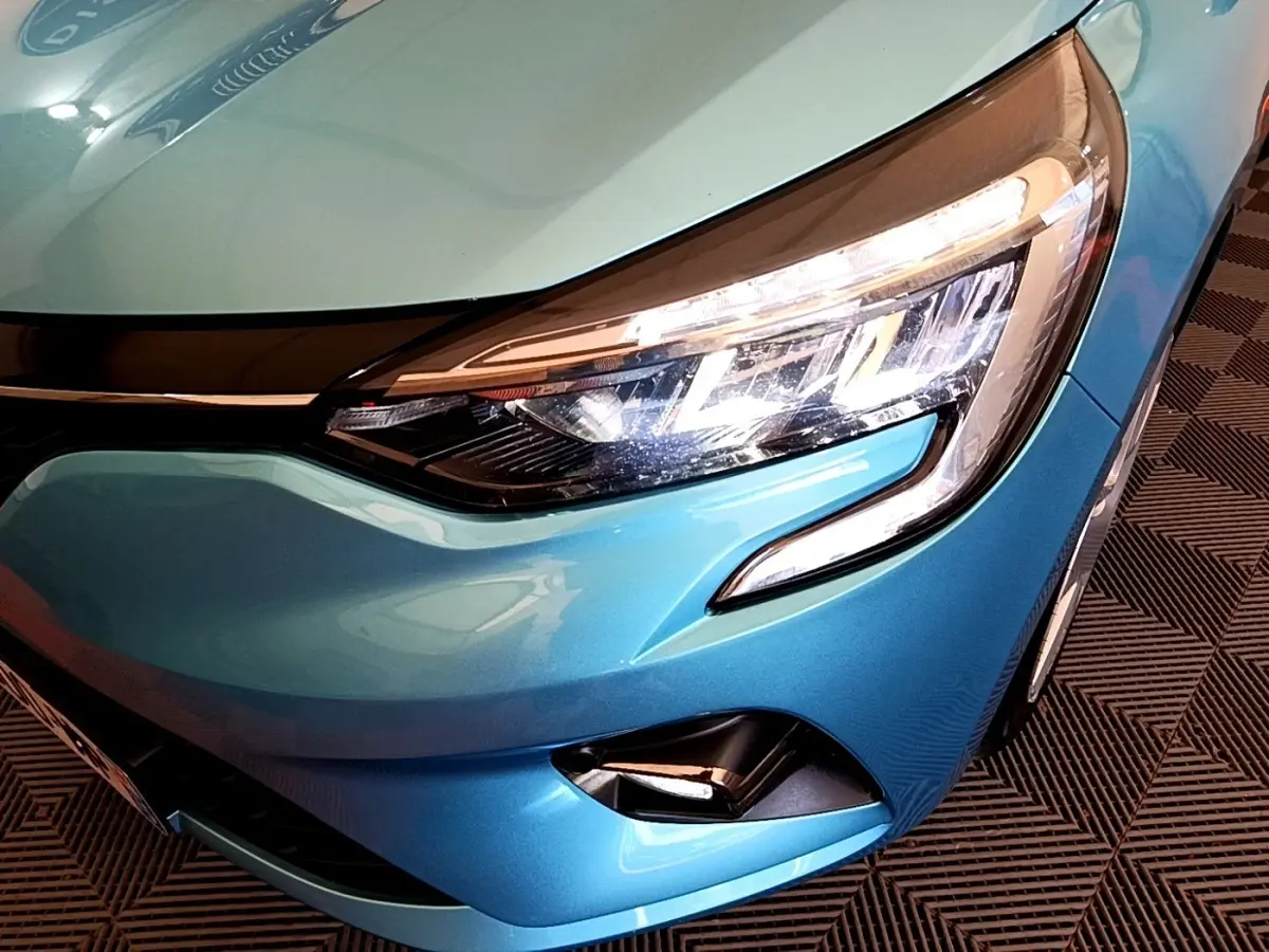Gros plan sur le phare avant droit d'une Renault Clio Business E-Tech hybride 2021 bleu métallisé, avec feux LED allumés.