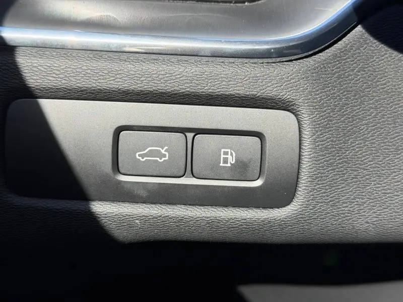 Boutons d'ouverture du coffre et de la trappe à carburant sur la planche de bord noire du Volvo XC60 gris 2024.
