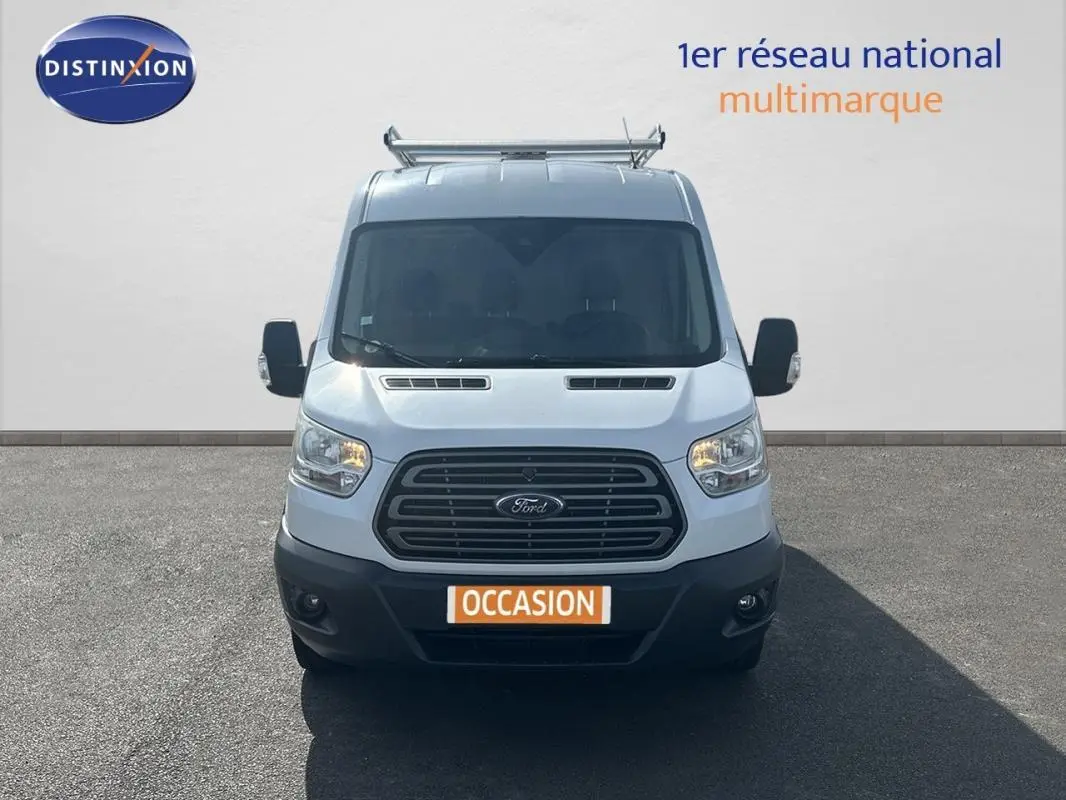 Vue de face du Ford Transit Fourgon blanc de 2015 avec calandre noire et phares allumés.
