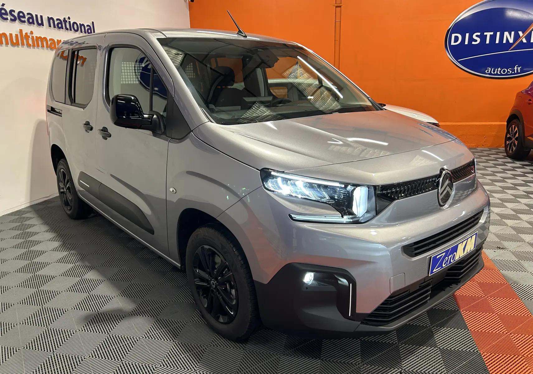 Vue 3/4 avant d'un Citroën Berlingo Multispace gris Artense avec phares allumés dans un showroom.
