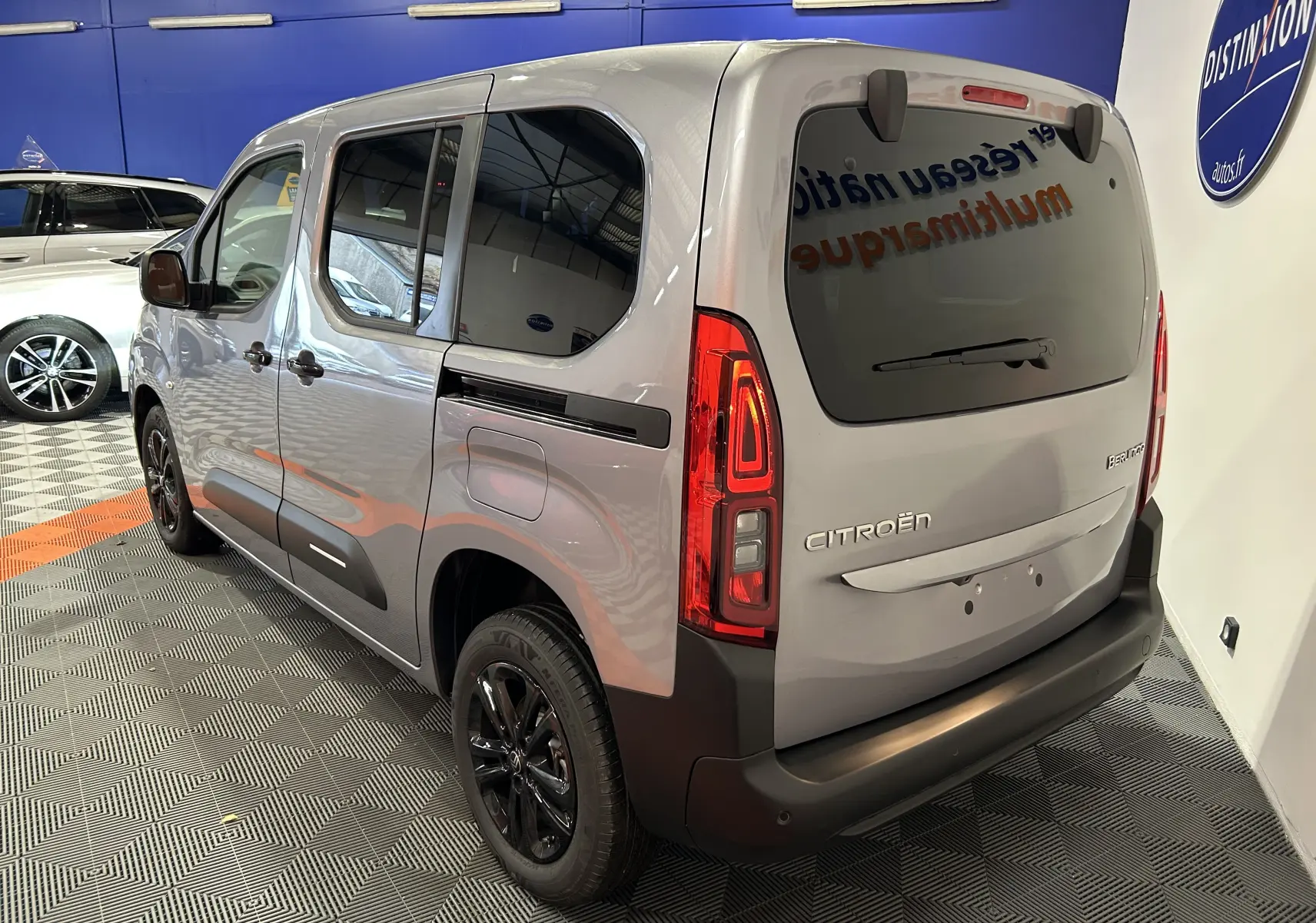 Vue 3/4 arrière droite du Citroën Berlingo Multispace gris Artense avec vitres teintées et jantes noires en intérieur showroom.