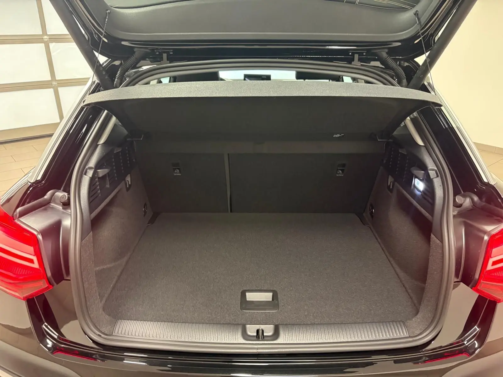 Coffre ouvert vu de l'arrière d'un Audi Q2 35 TFSI S Line noir Mythic, montrant l'espace de chargement vide et l'éclairage intérieur.