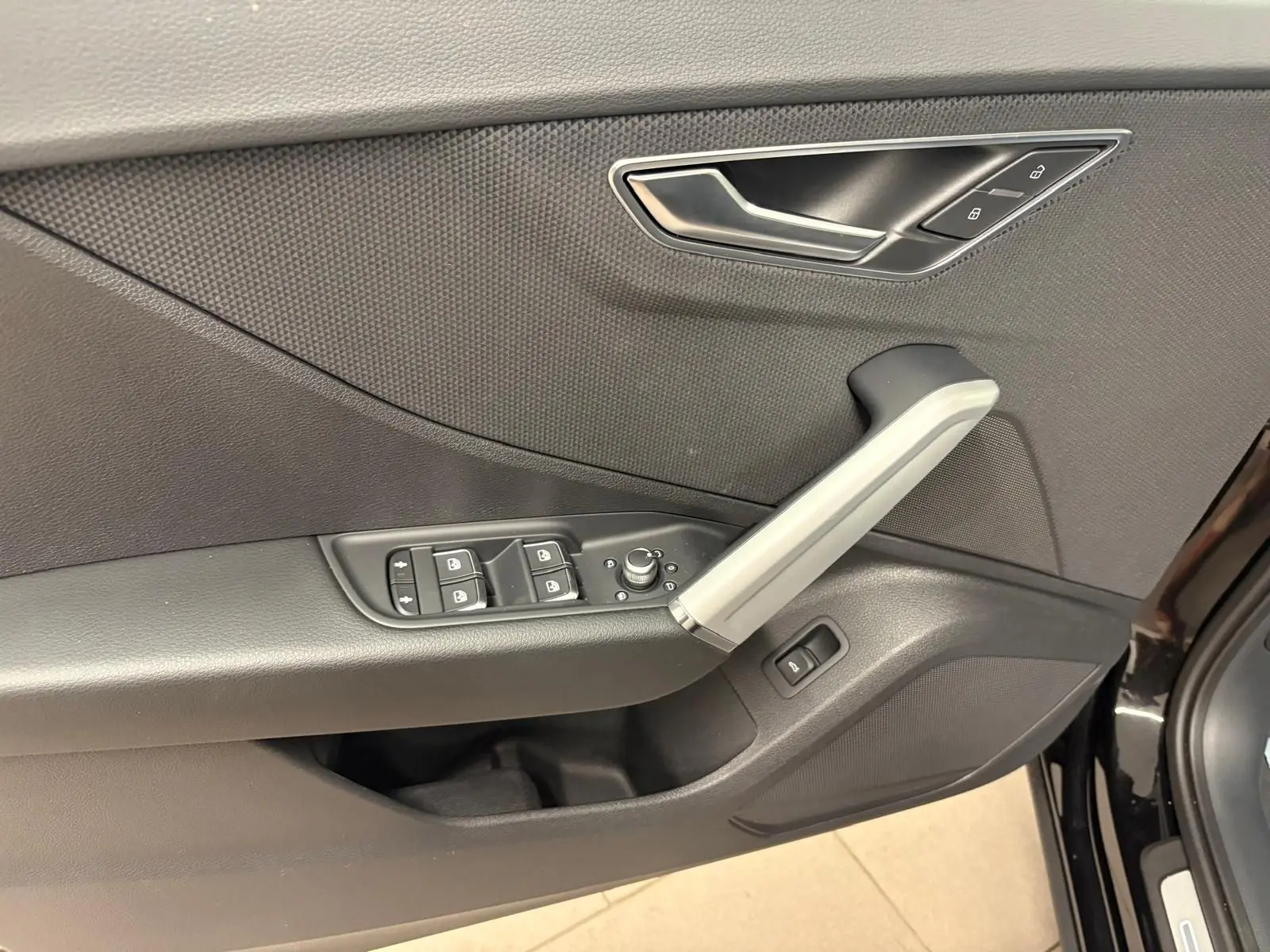 Gros plan sur la porte avant gauche de l'Audi Q2 Noir Mythic, montrant les commandes des vitres et la poignée intérieure grise.